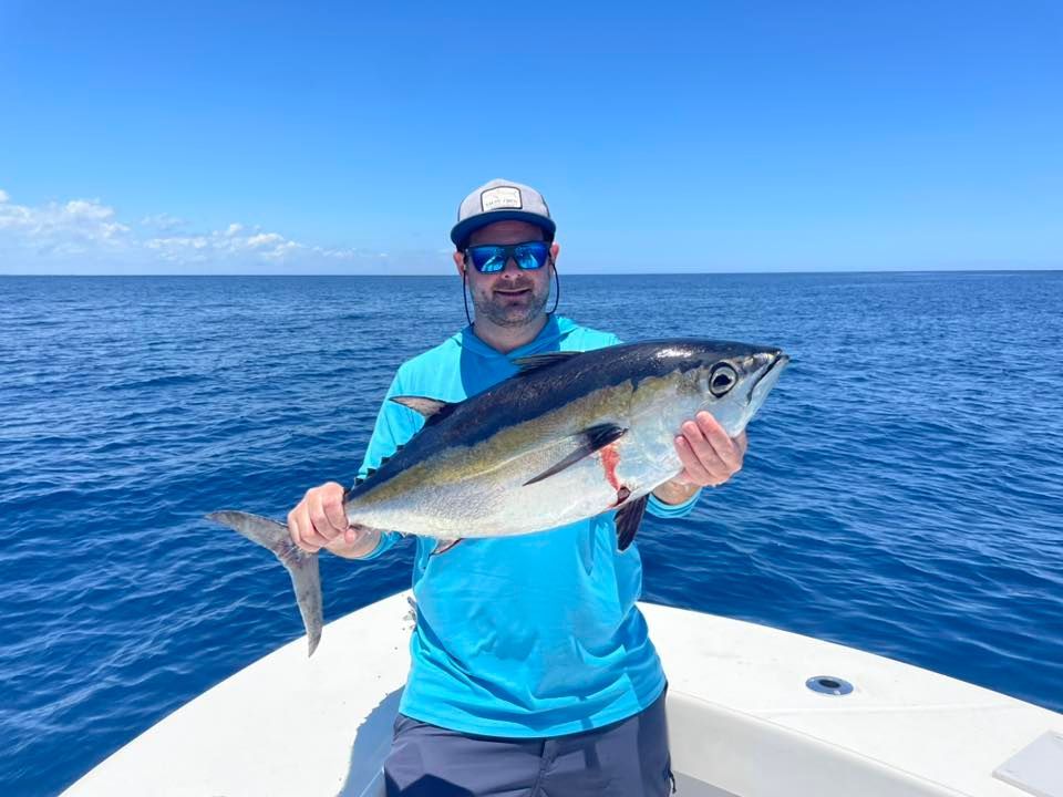 Person on a boat holding a large fish against a blue ocean and sky