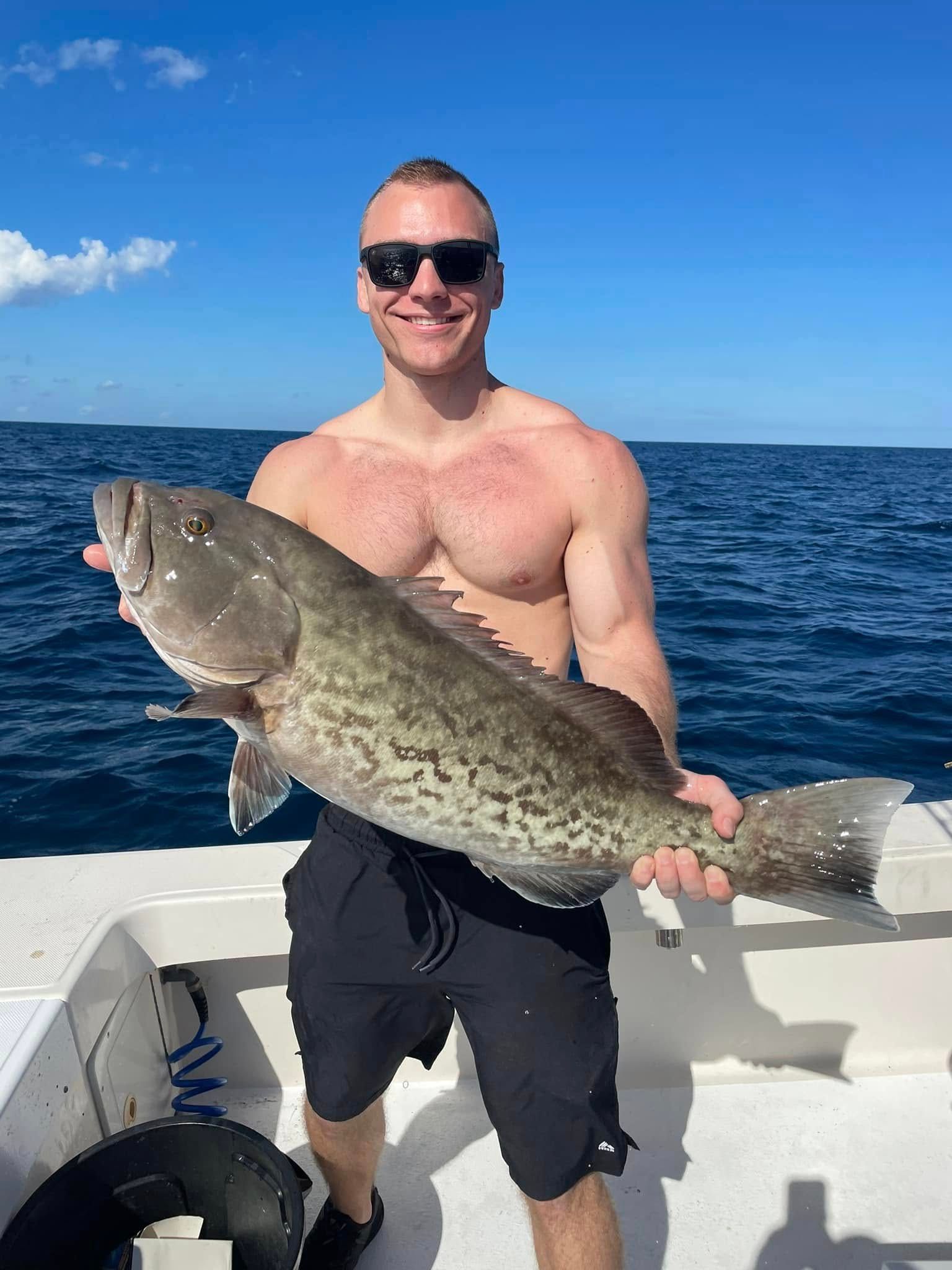 Man on a boat holding a large fish, with open ocean and blue sky in the background