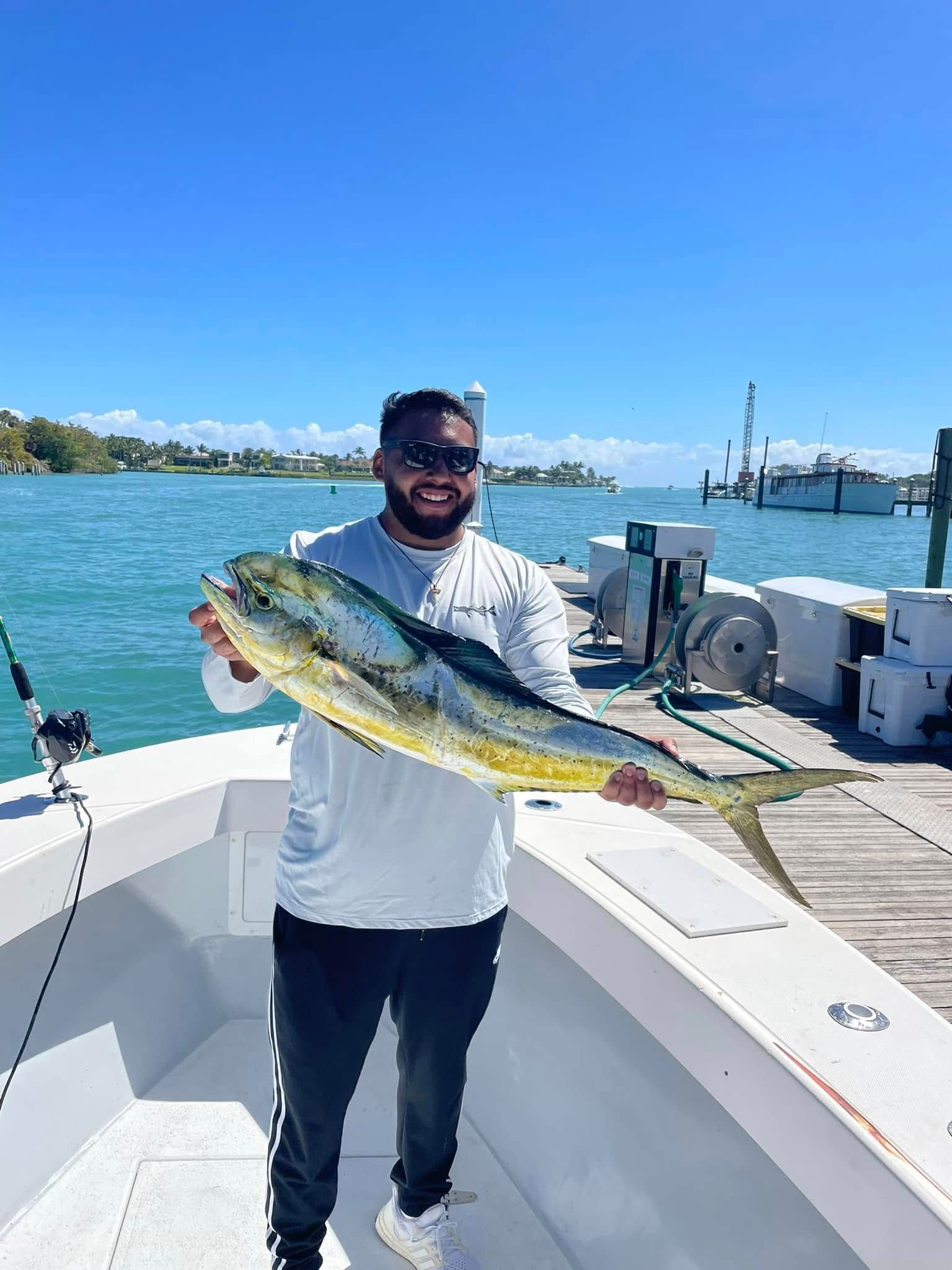 Man on a boat holding a large fish with a marina and blue water in the background