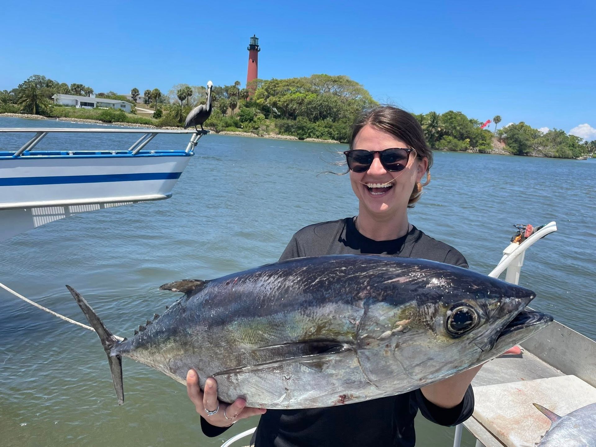 Person holding a large fish on a boat, with a red lighthouse and water in the background.