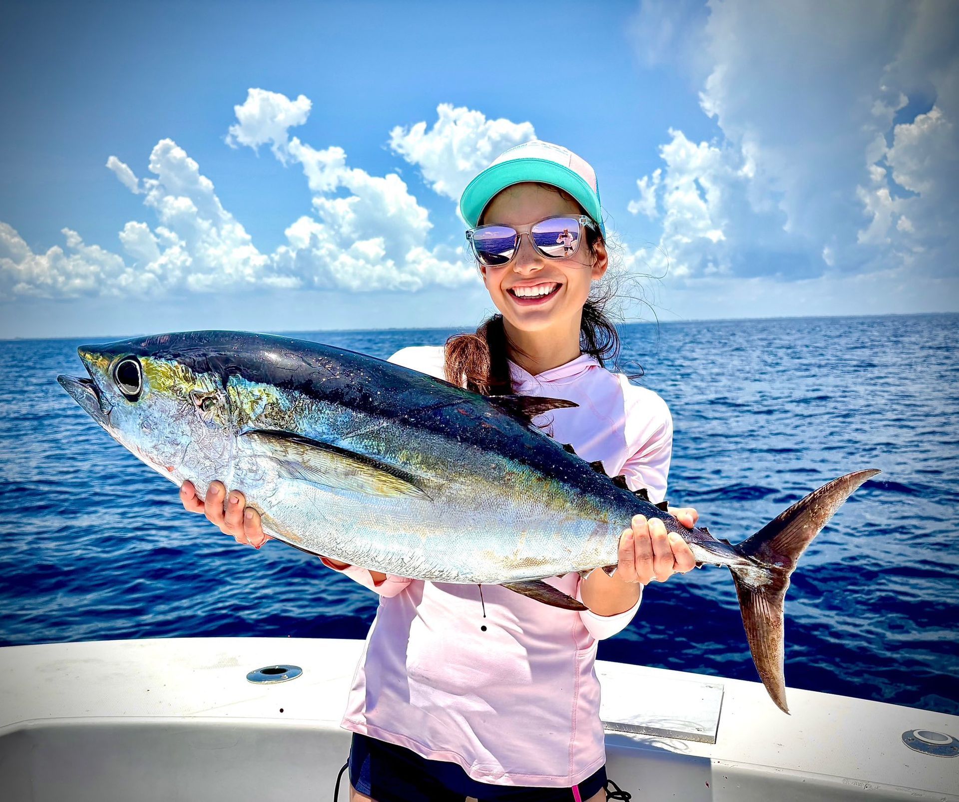 Smiling angler holds a large tuna on a boat with blue ocean and sky behind her