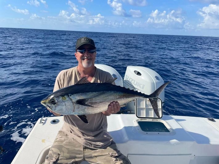 Man holding a large fish on a boat at sea under a blue sky