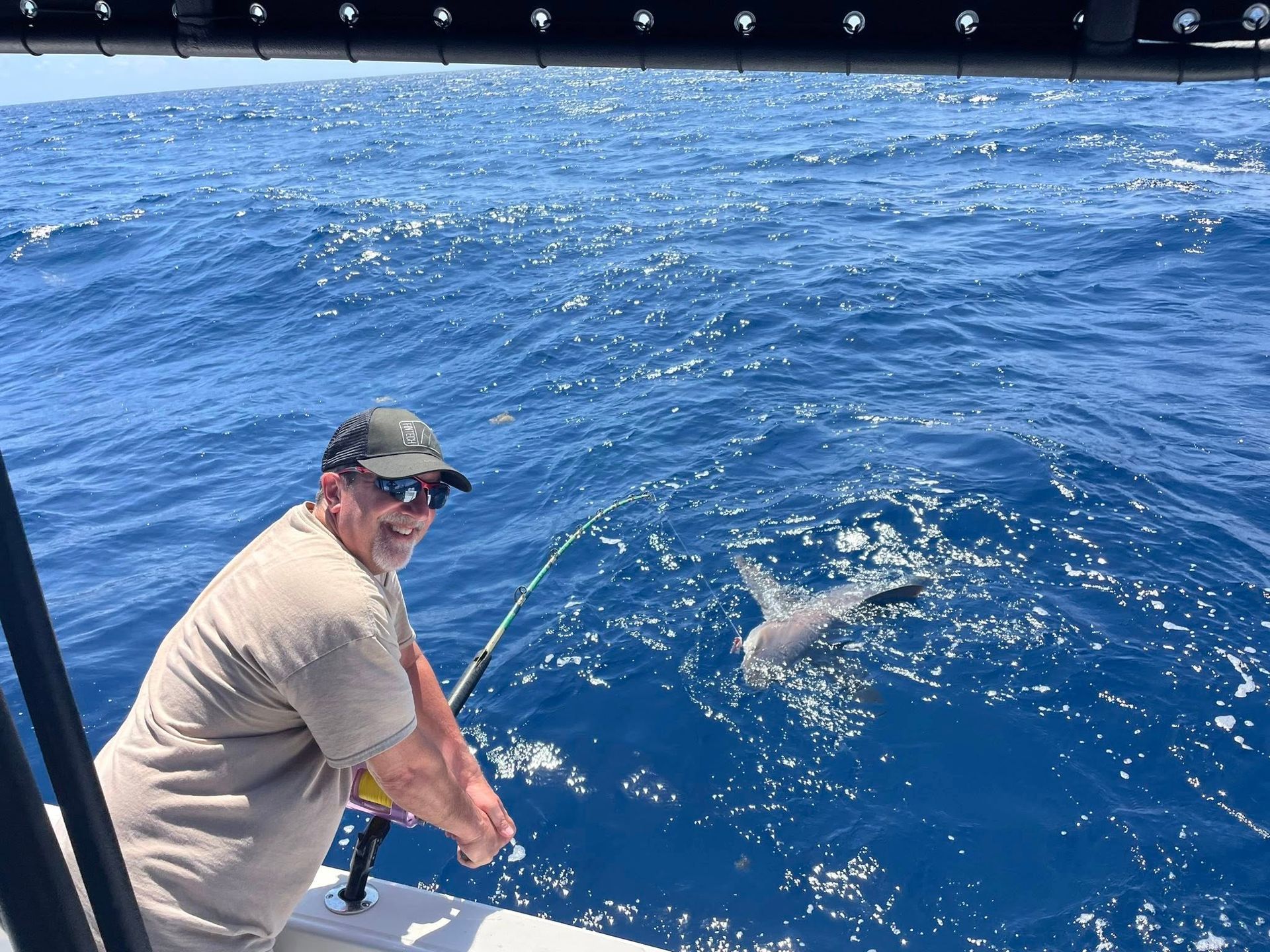 Man on a boat reels in a fish in blue open water
