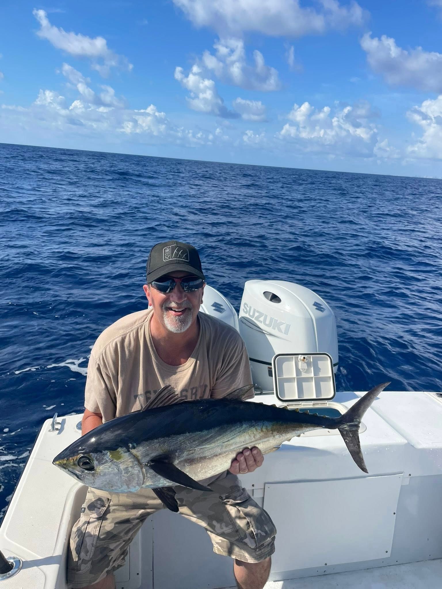 Man holding a large fish on a boat in open ocean under a partly cloudy sky