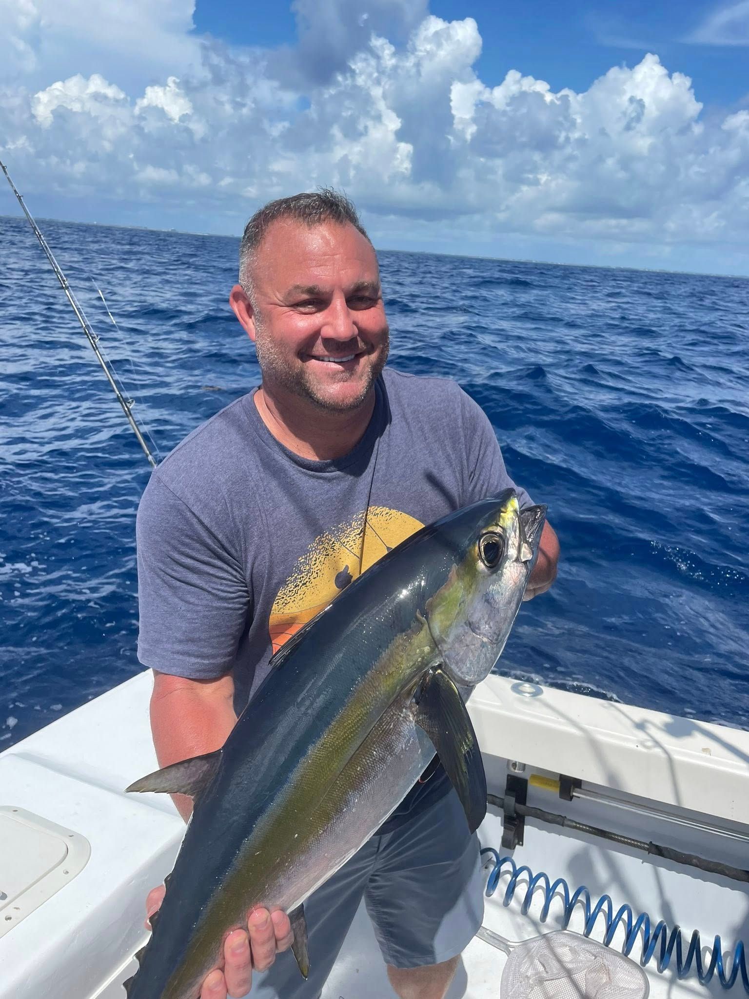 Man on a boat holding a large yellow-and-silver fish on a bright blue ocean