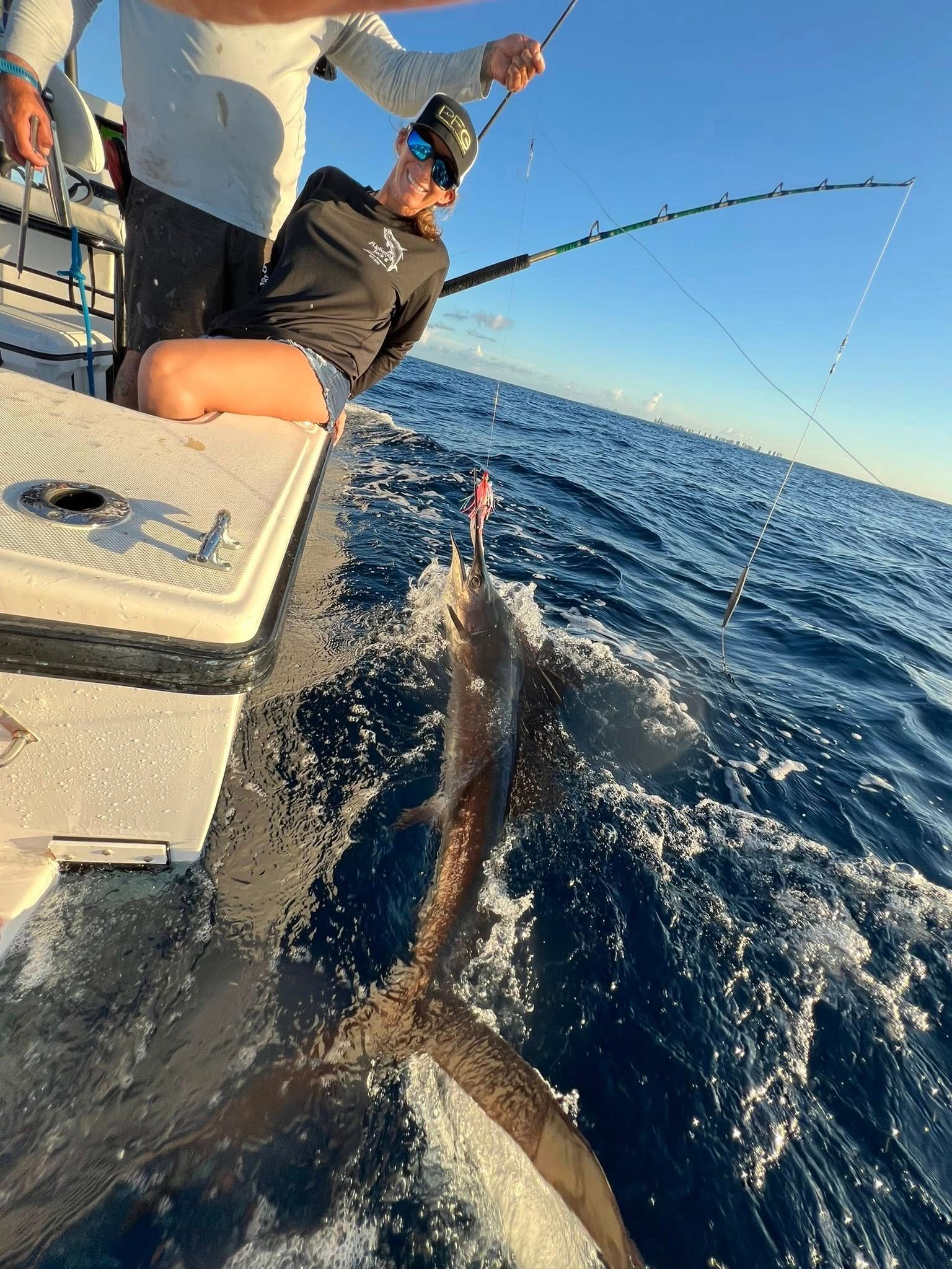 People fishing from a boat as a large shark thrashes beside the hull on a sunny ocean