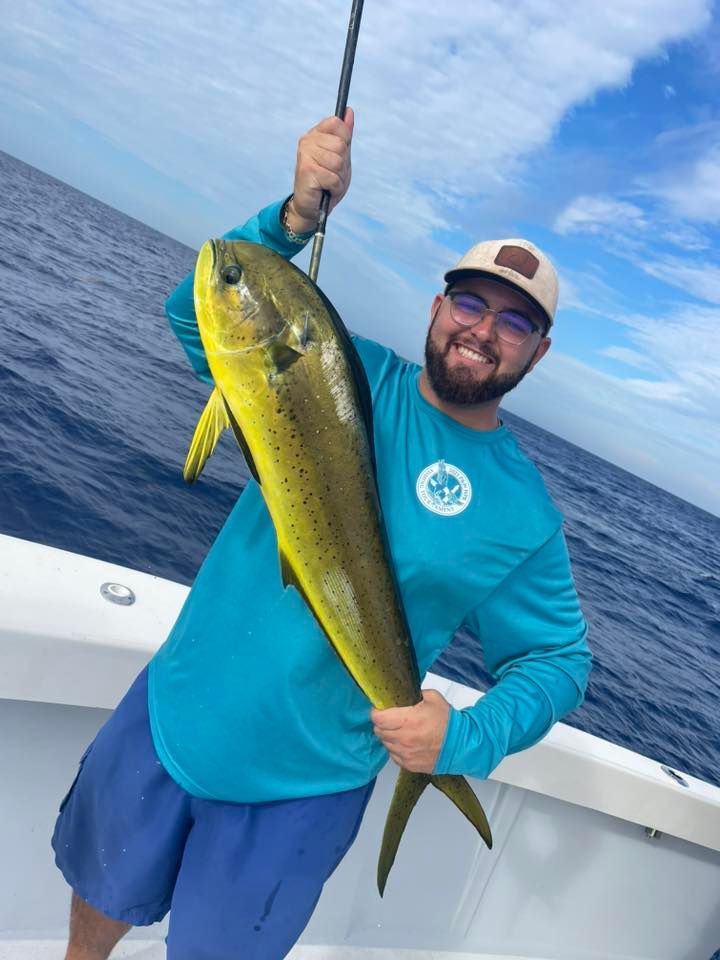 Man on a boat holding up a large yellow-green fish over the ocean