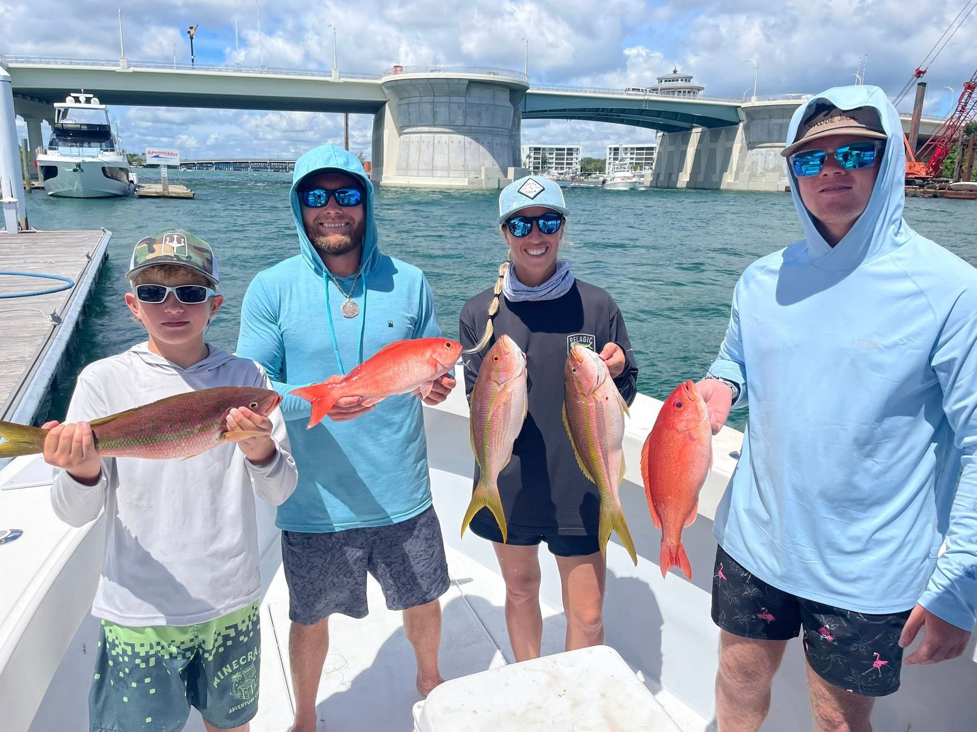 Four people on a boat holding up caught fish with a bridge in the background