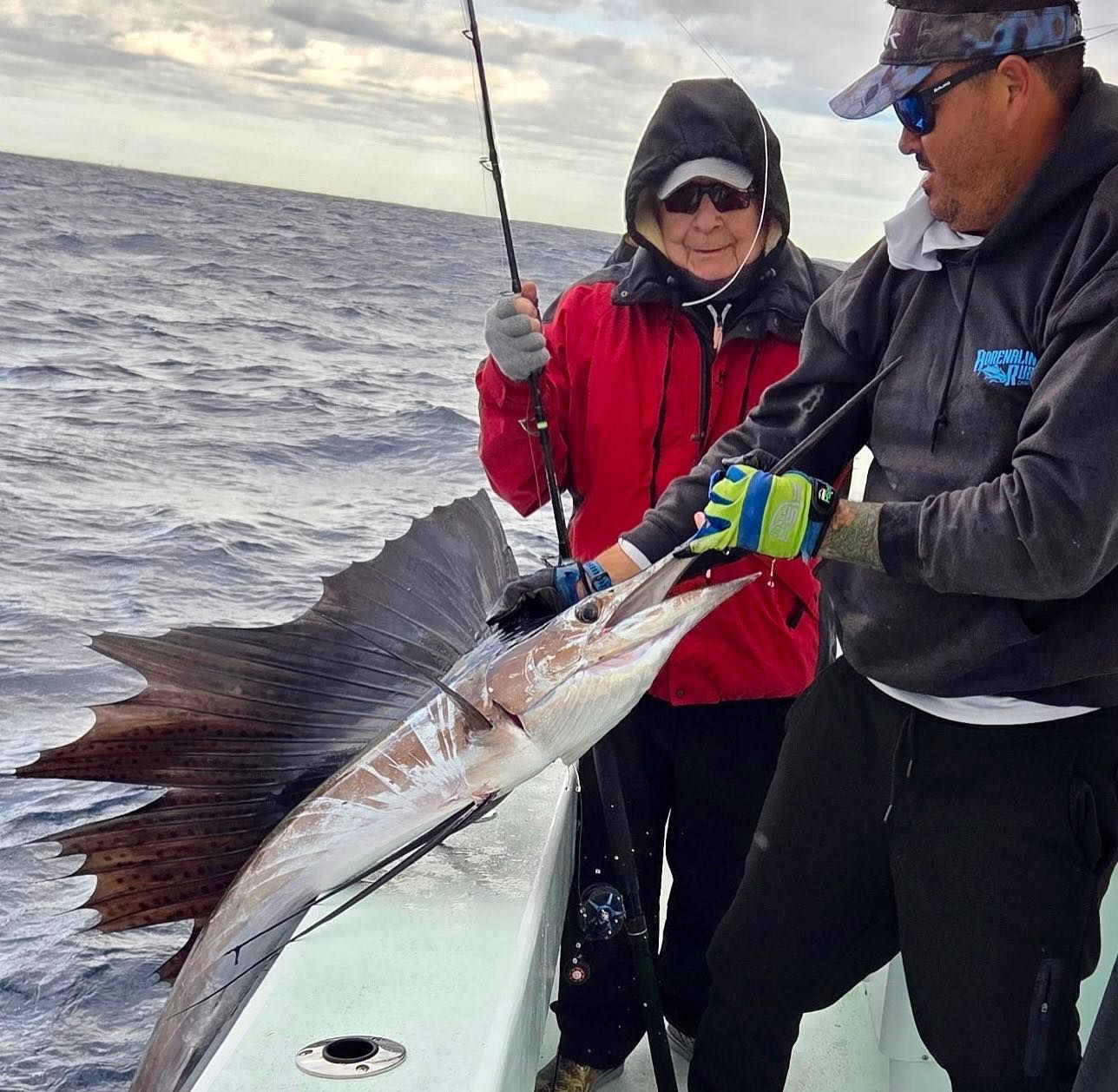 Two anglers on a boat hold a large fish beside the rail on a choppy sea.