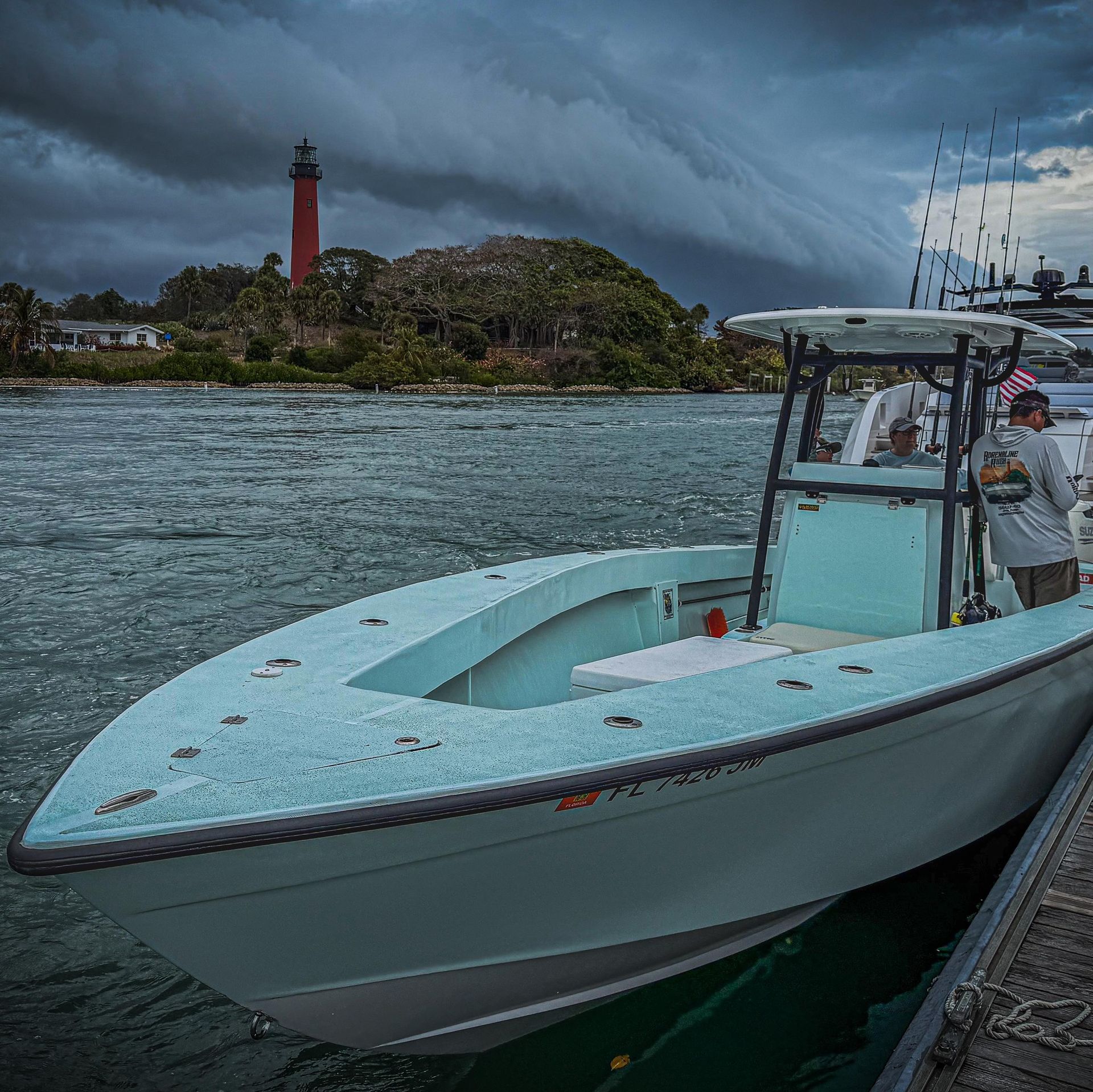 Light blue boat at a dock with a red lighthouse across choppy water under stormy skies