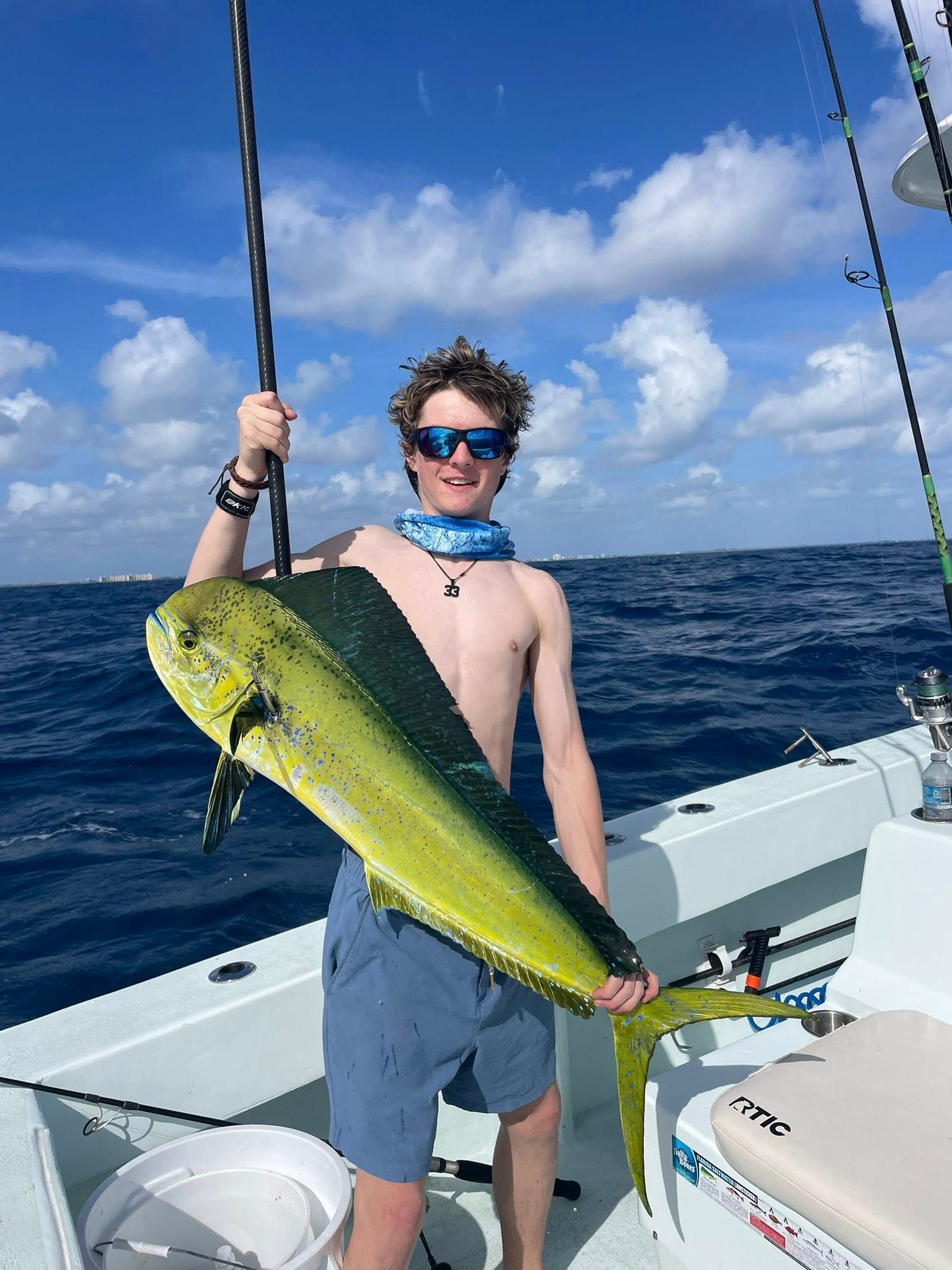 Person on a boat holding a large yellow-green fish against a blue ocean and sky.