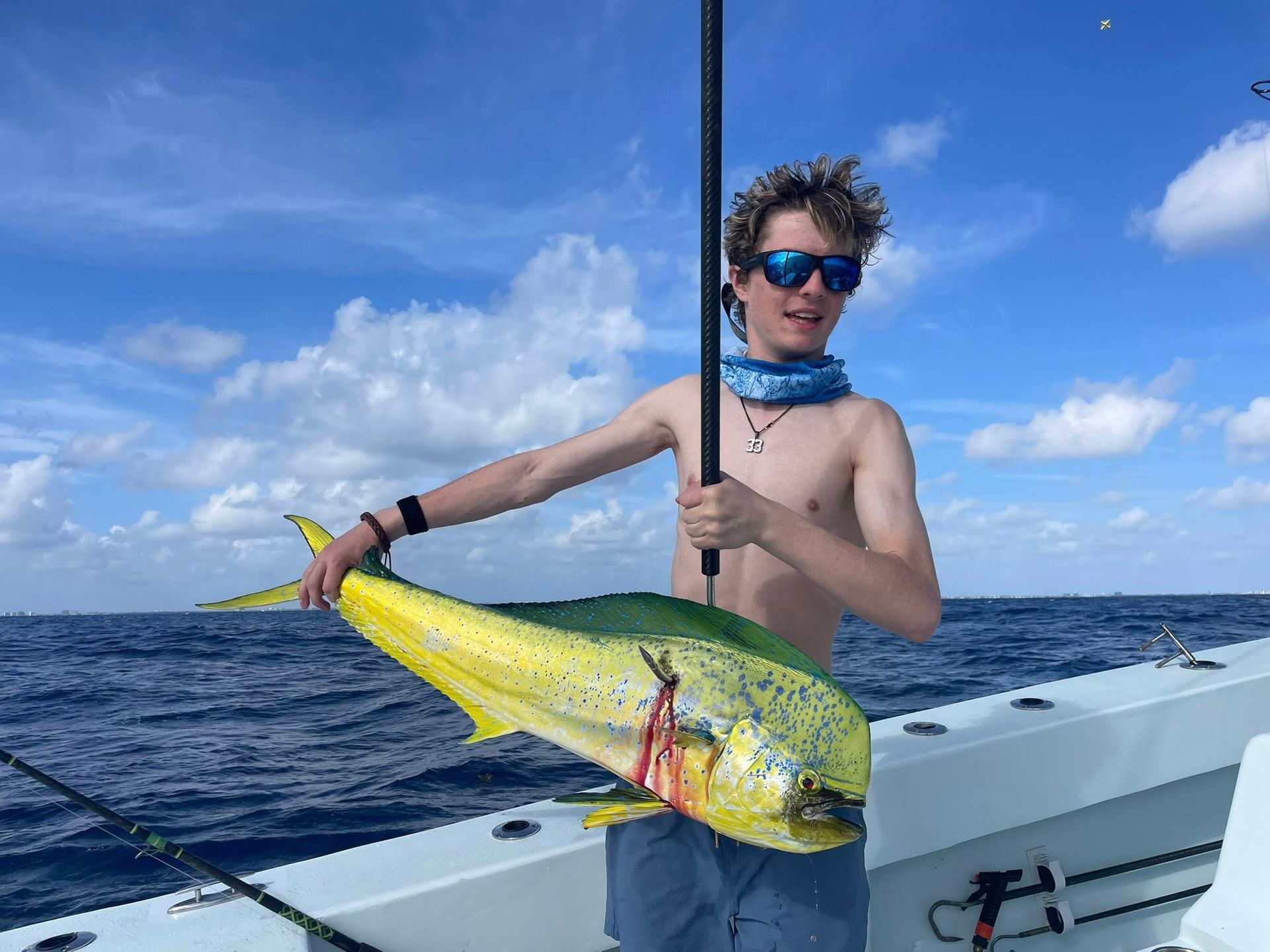 Person on a boat holding a large yellow fish on a sunny ocean day