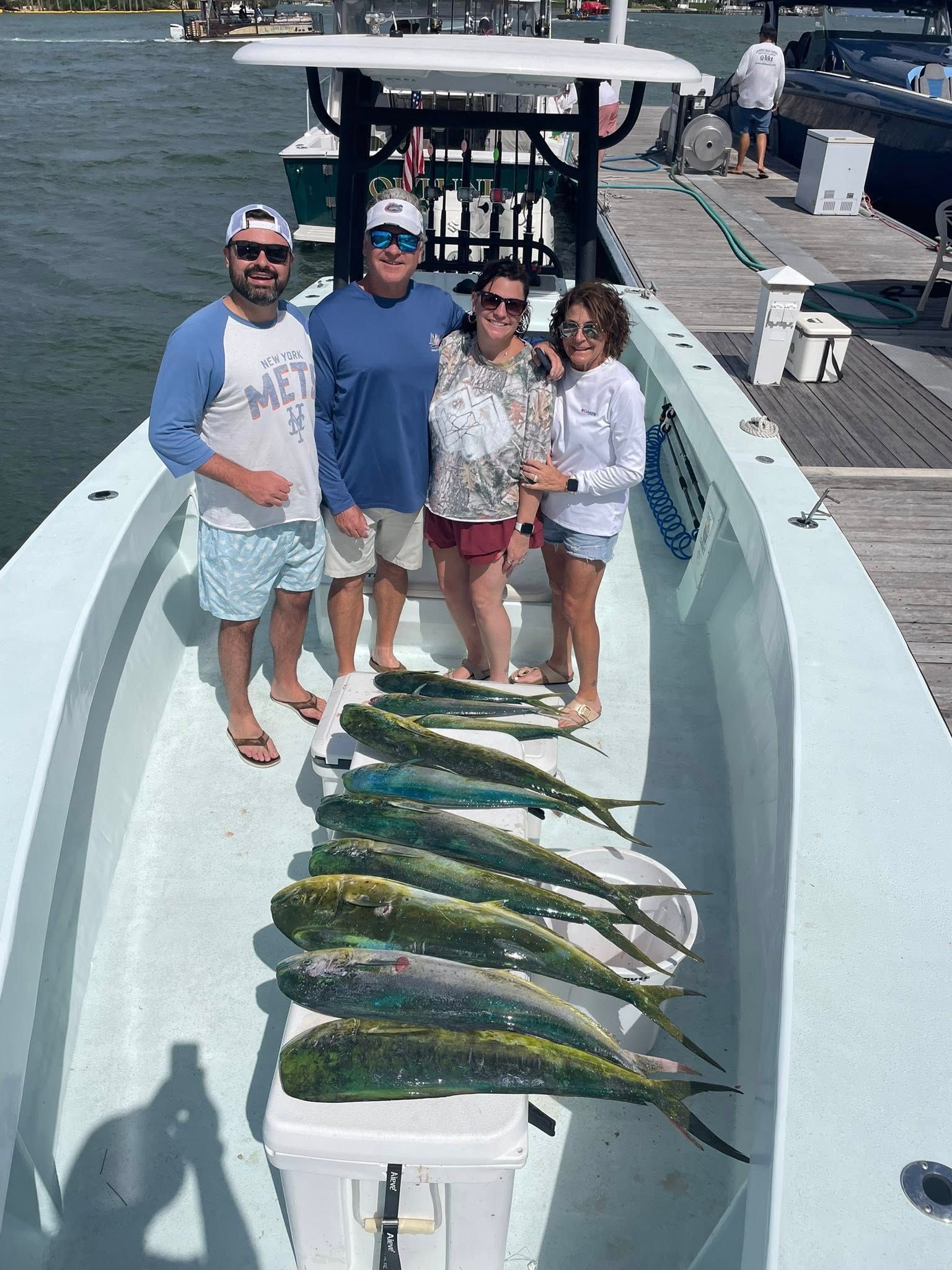 Four people posing on a boat with a row of freshly caught fish on the deck