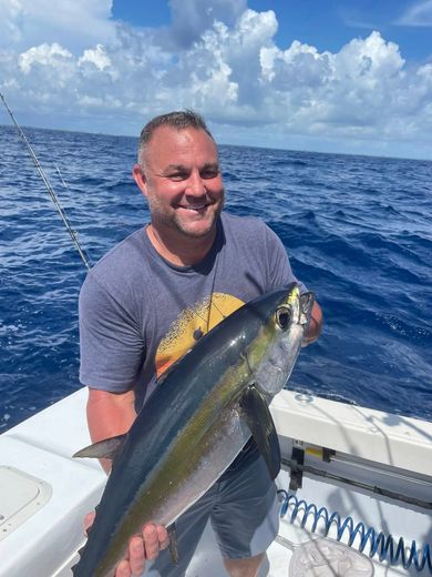 Man on a boat holding a large fish against a blue ocean and cloudy sky