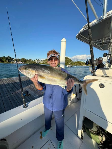 Person on a boat holding a large fish, with blue water and clear sky in the background.