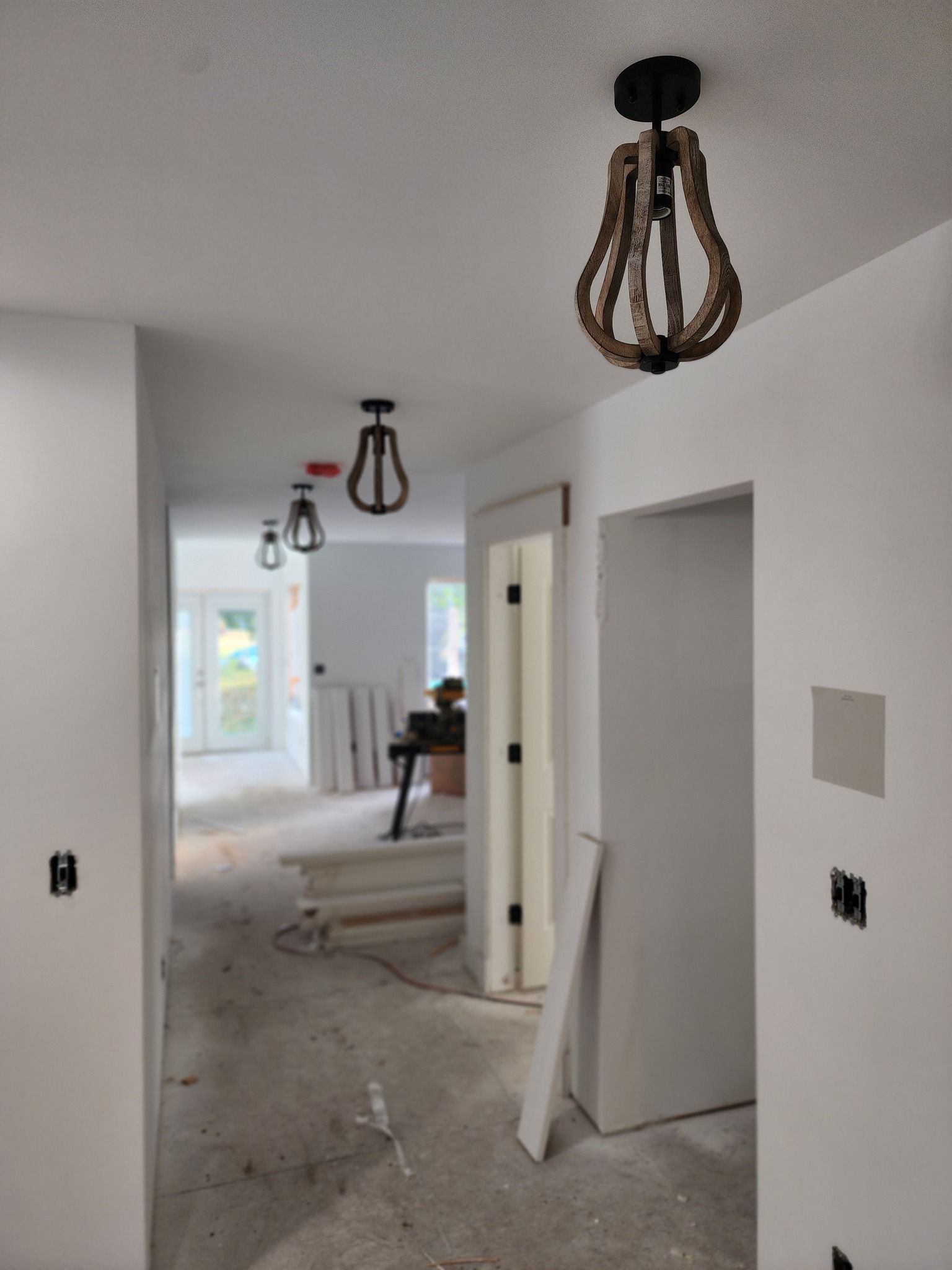 A hallway with three wooden-framed pendant lights hanging from the ceiling. The walls are white and under construction.