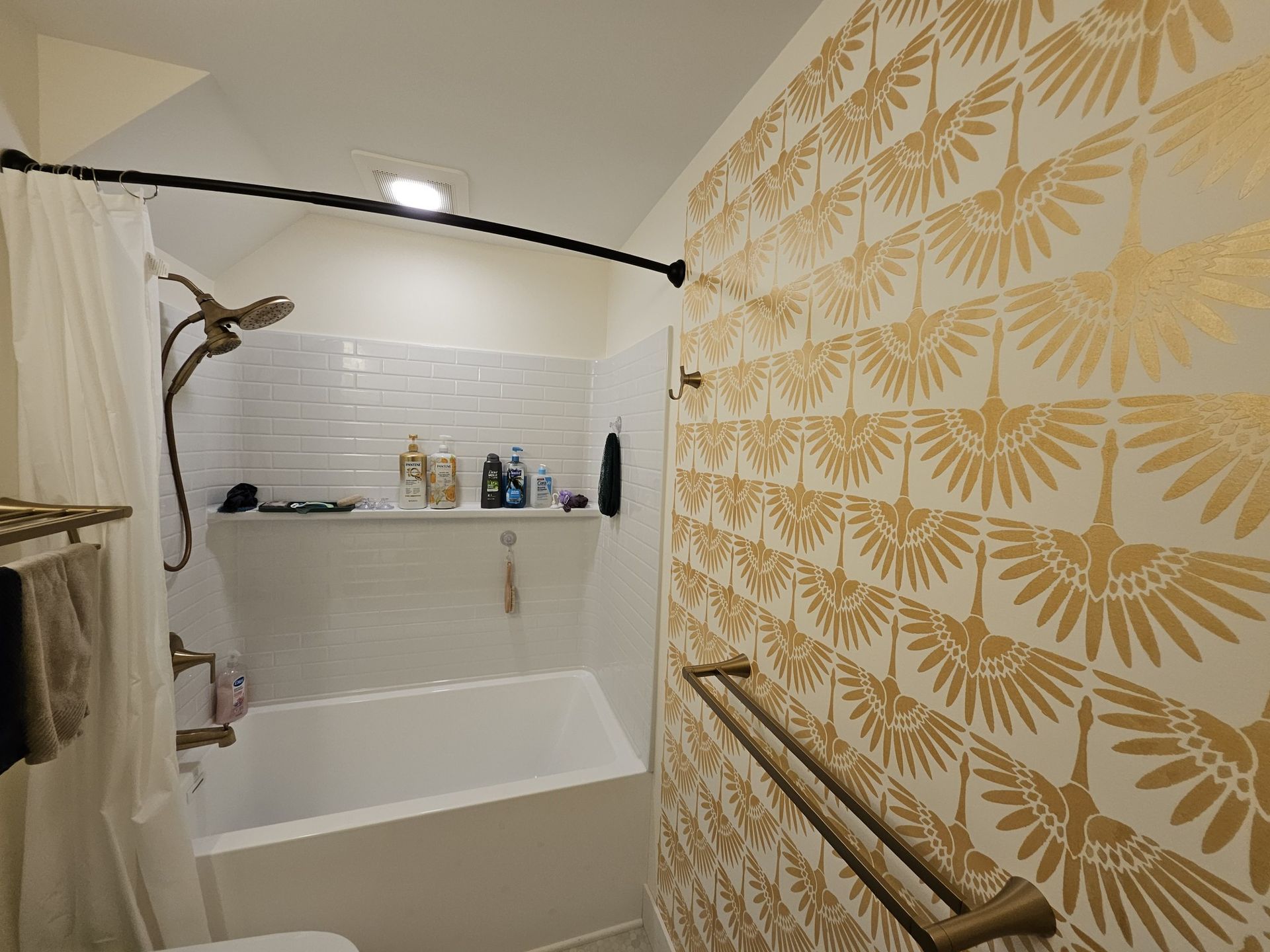 Bathroom with white subway tile, a gold patterned accent wall, and bronze fixtures. Shower has a curved rod and a tub.