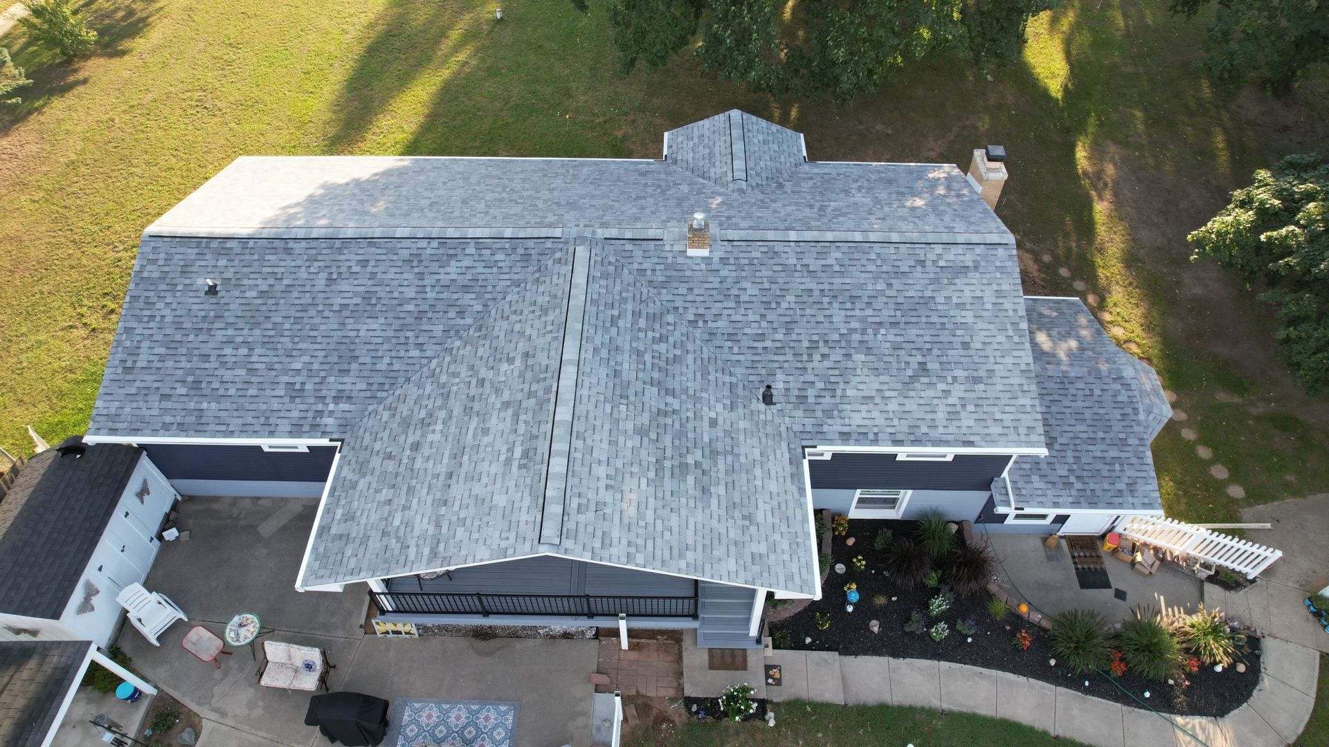 Aerial view of a house with a gray roof, blue siding, and a landscaped yard with a winding walkway.