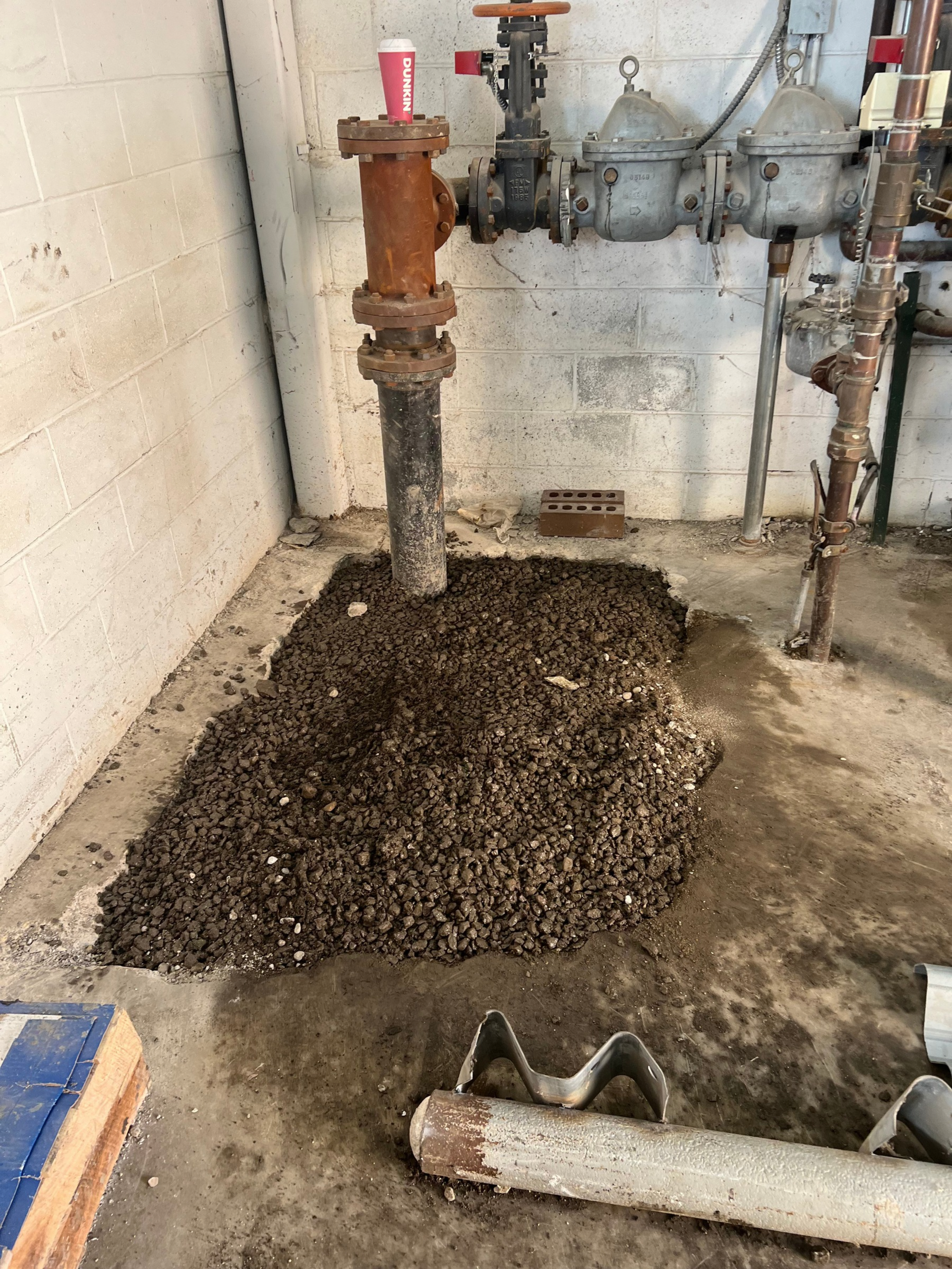 Utility room with exposed pipes, a large pile of dirt on the floor, and a drain pipe in the foreground