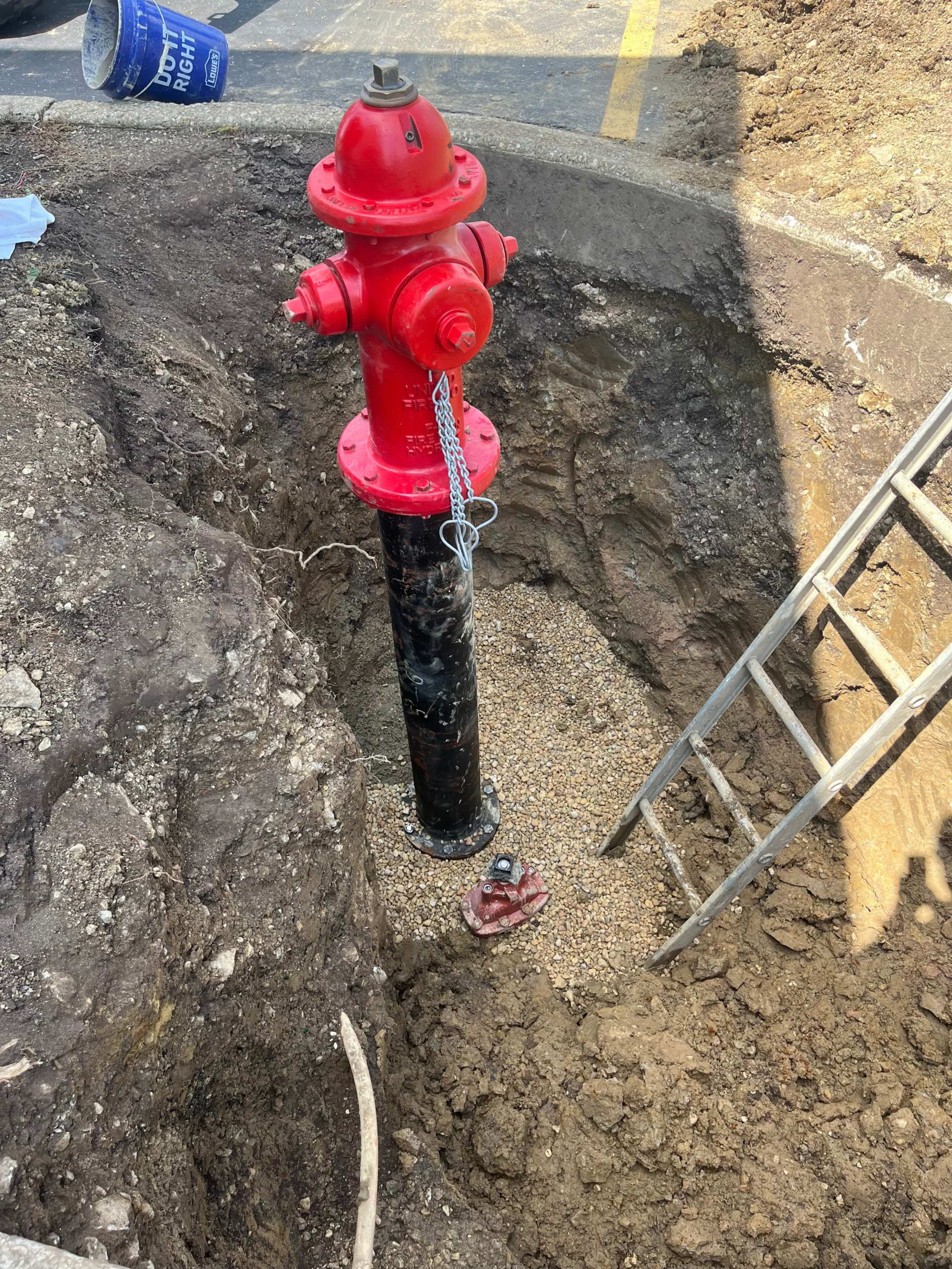 Red fire hydrant on a black pipe in a muddy construction excavation beside a road lane line
