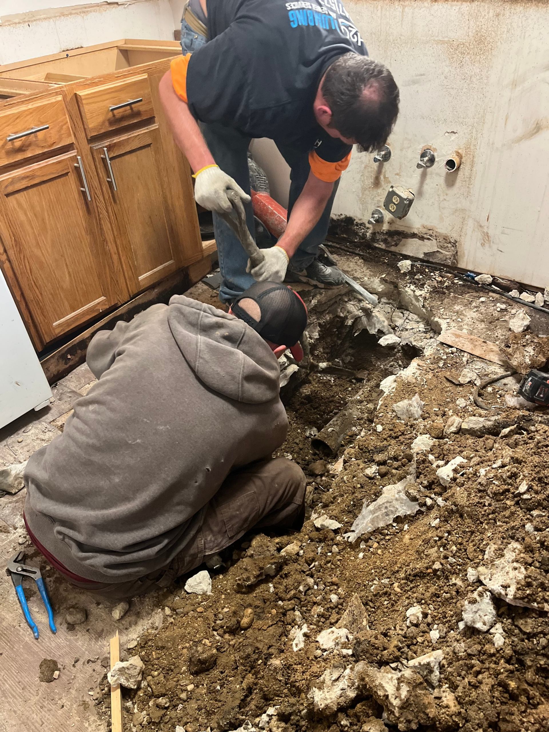 Workers clear debris and damaged flooring in a kitchen during a renovation or cleanup.