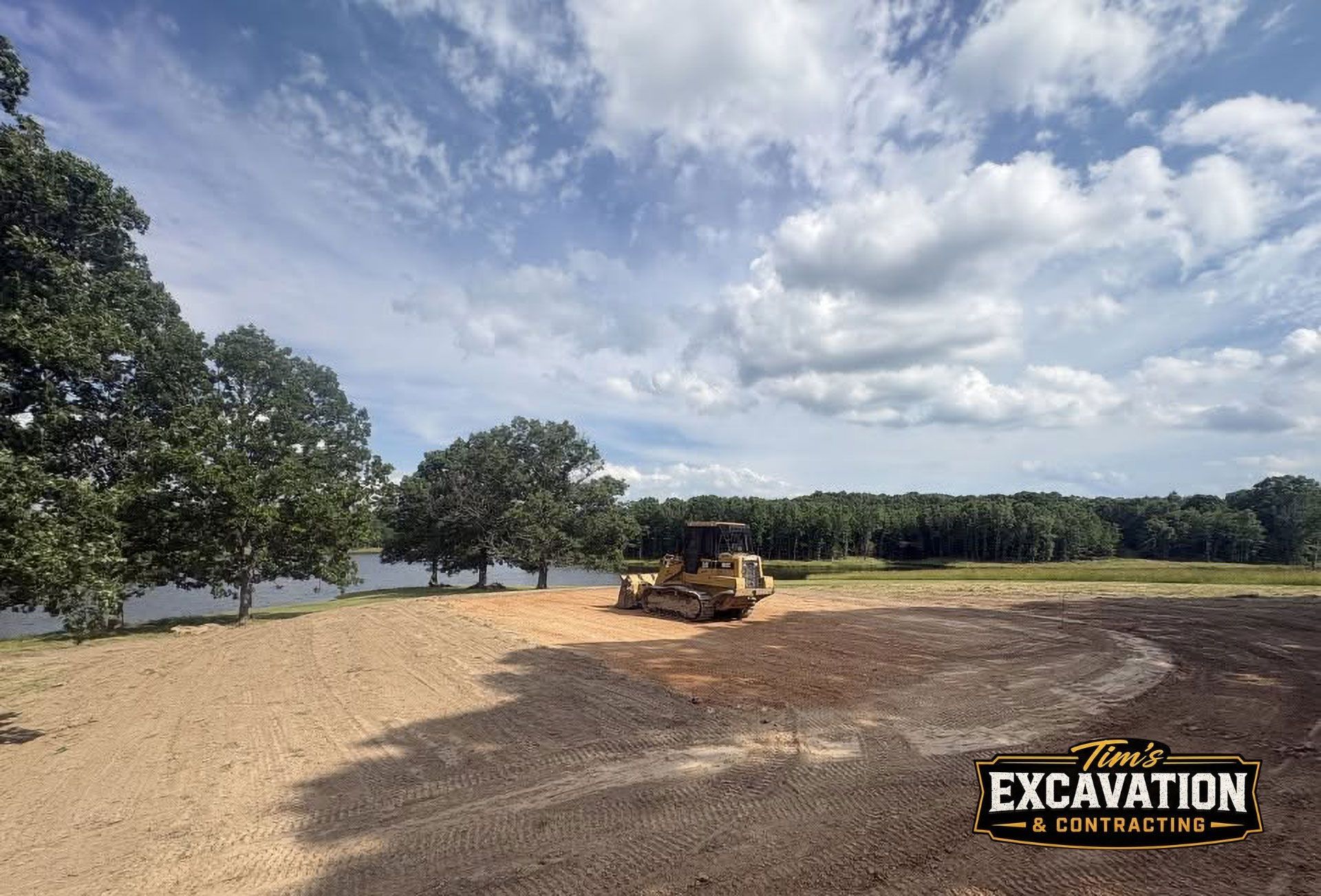 Excavator grading a sandy lot under a cloudy sky with trees in the background