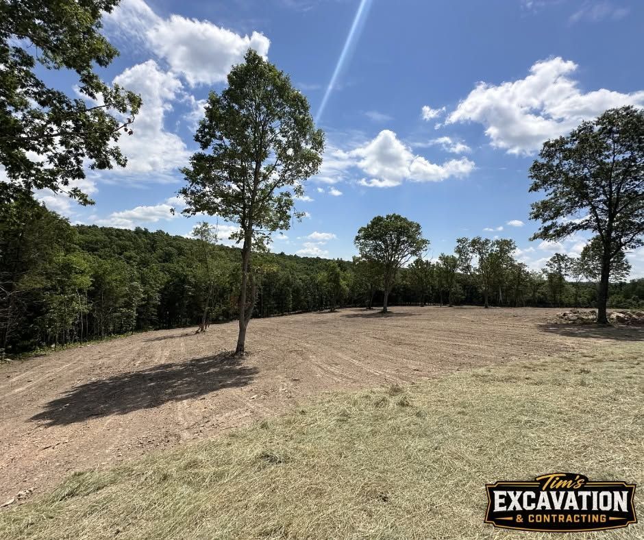 Cleared dirt lot with scattered trees under a blue sky and clouds, marked by an excavation sign