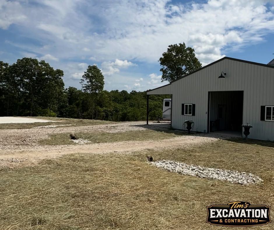 Gravel lot beside a white metal building under a partly cloudy sky, with trees in the background