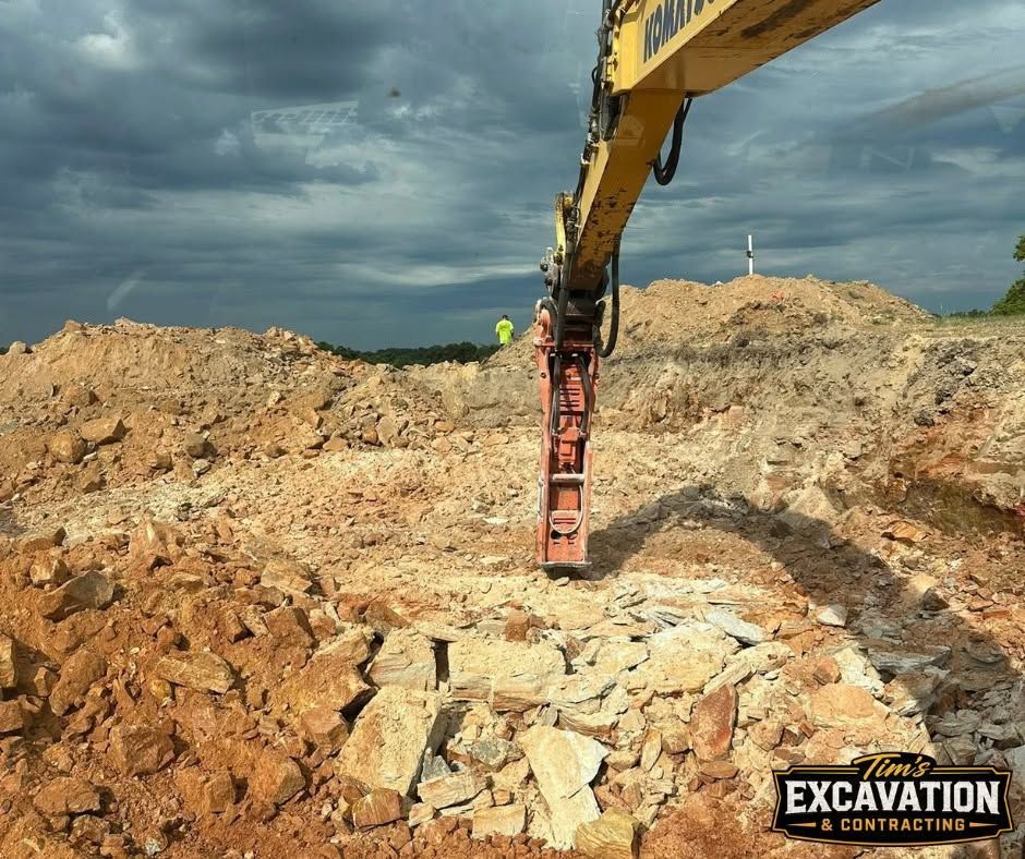 Excavator arm breaking rock at a construction site under dark clouds