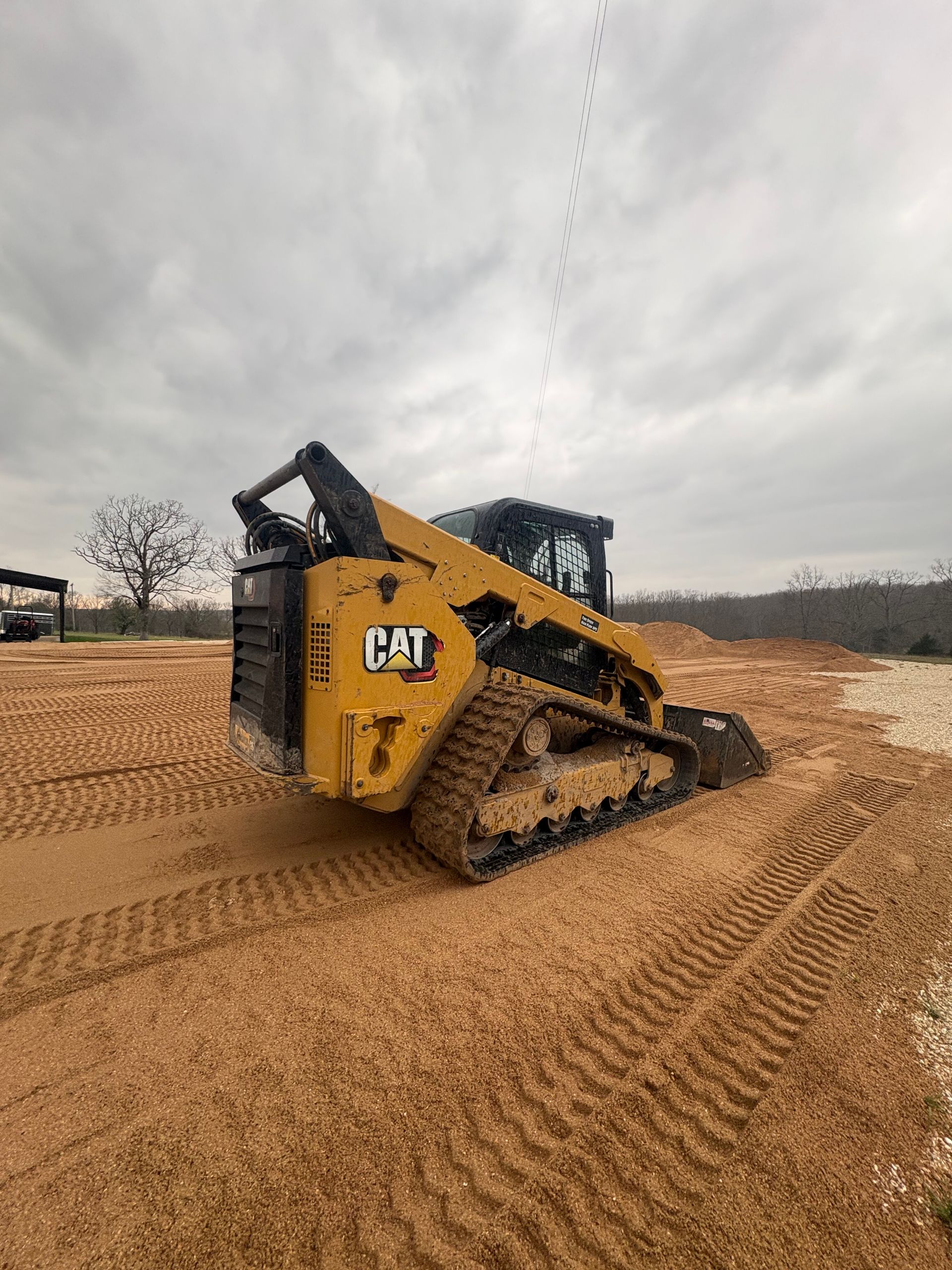 Yellow CAT compact track loader driving through muddy field under cloudy sky