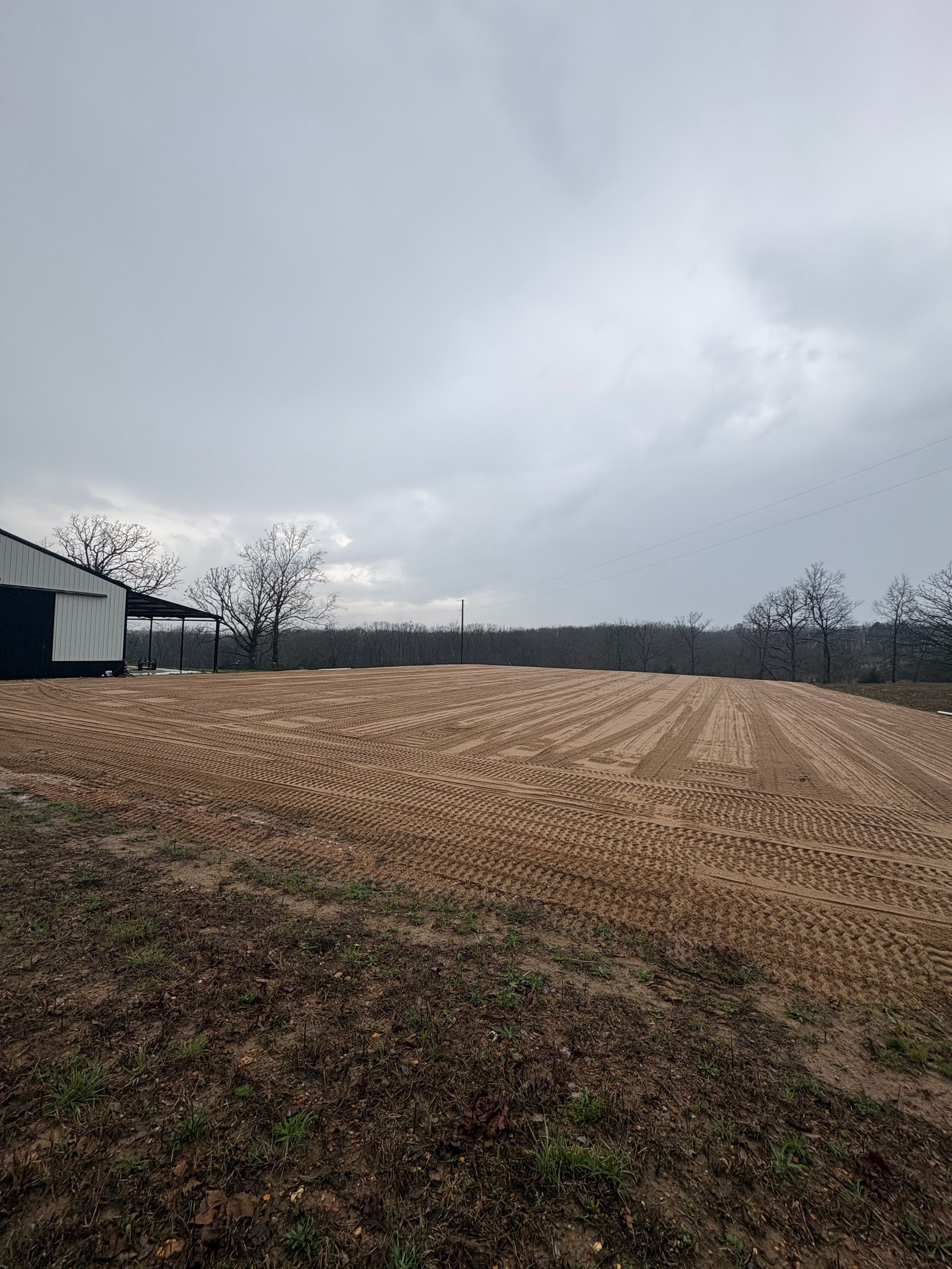 Overcast rural field with a freshly tilled brown hillside and a barn at left