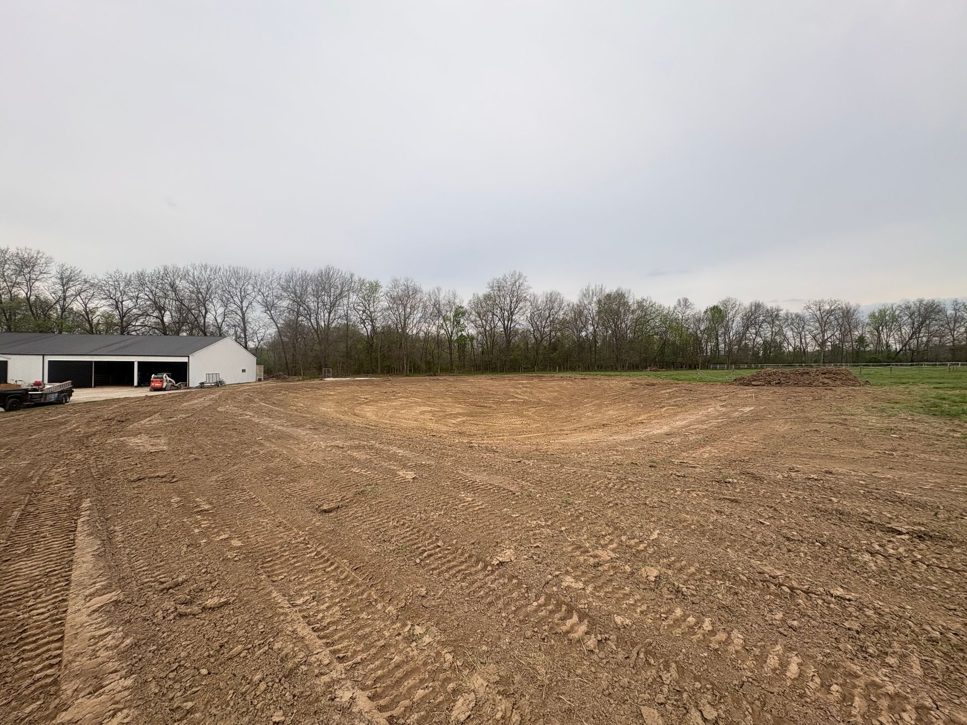 Freshly plowed brown field beside a small white barn under an overcast sky