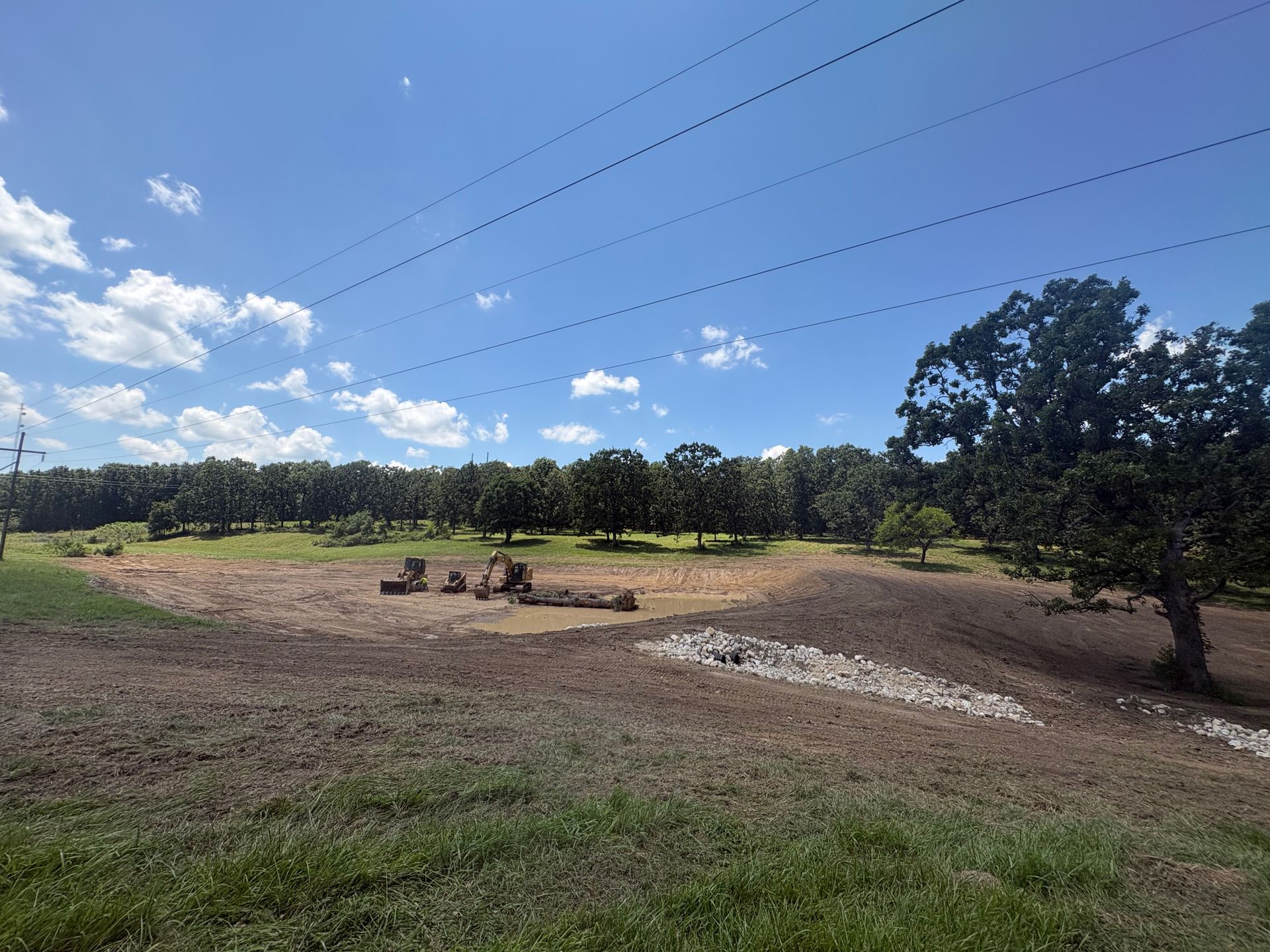 Dry, open field with small hay bales, scattered trees, and a bright blue sky with clouds.