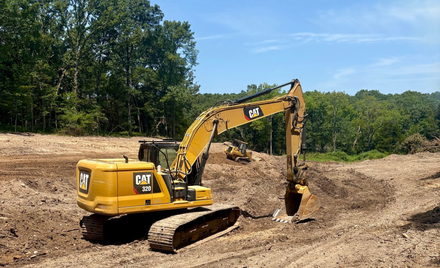 Yellow CAT bulldozer grading muddy dirt lot near a barn under a gray sky
