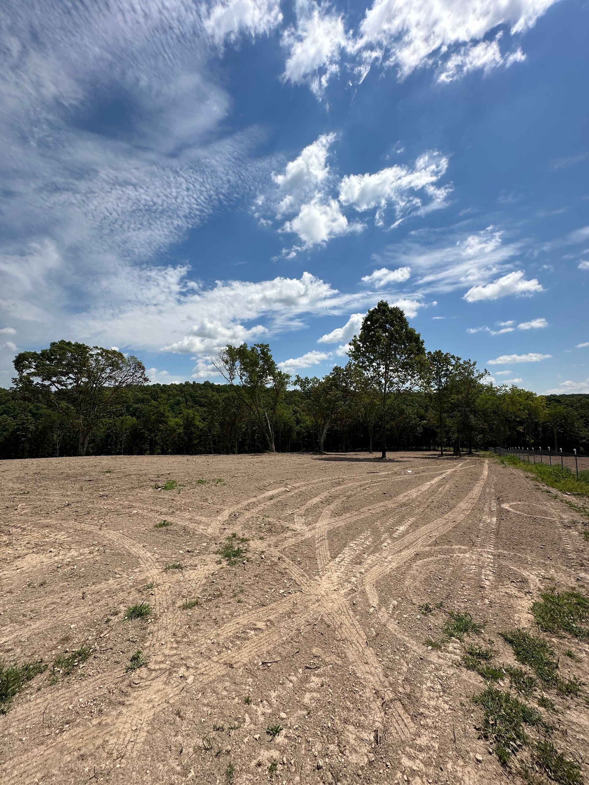 Plowed field under a blue sky with scattered clouds and a line of trees at the horizon