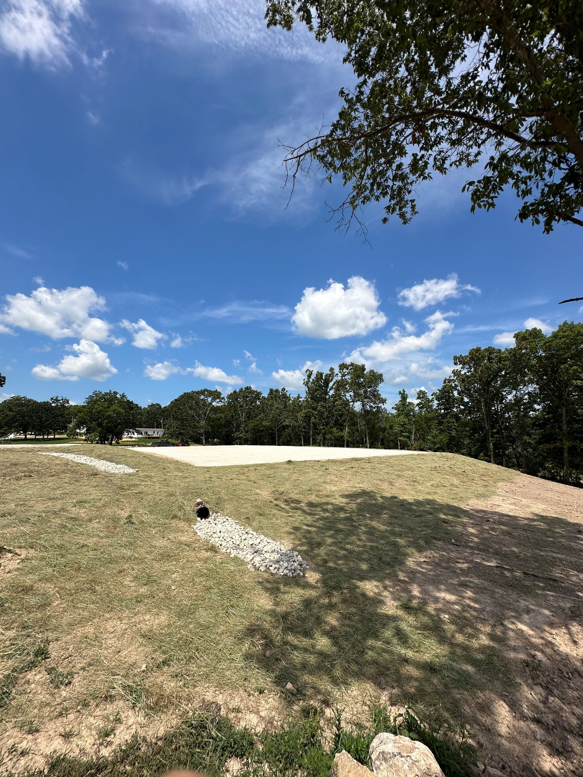 Grassy hill under a bright blue sky with scattered clouds and trees in the distance