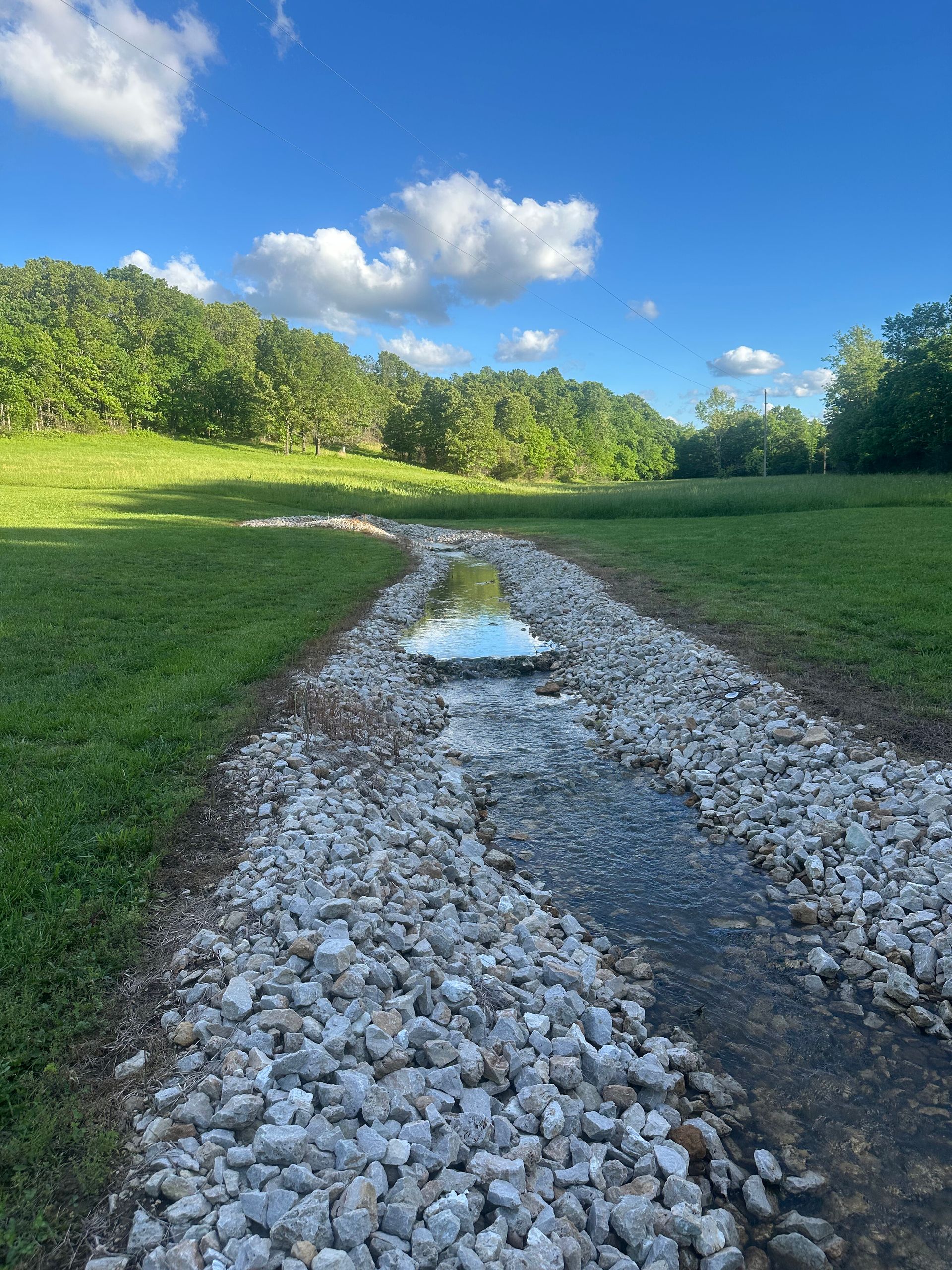Gravel path with puddles through a green field under a bright blue sky with clouds