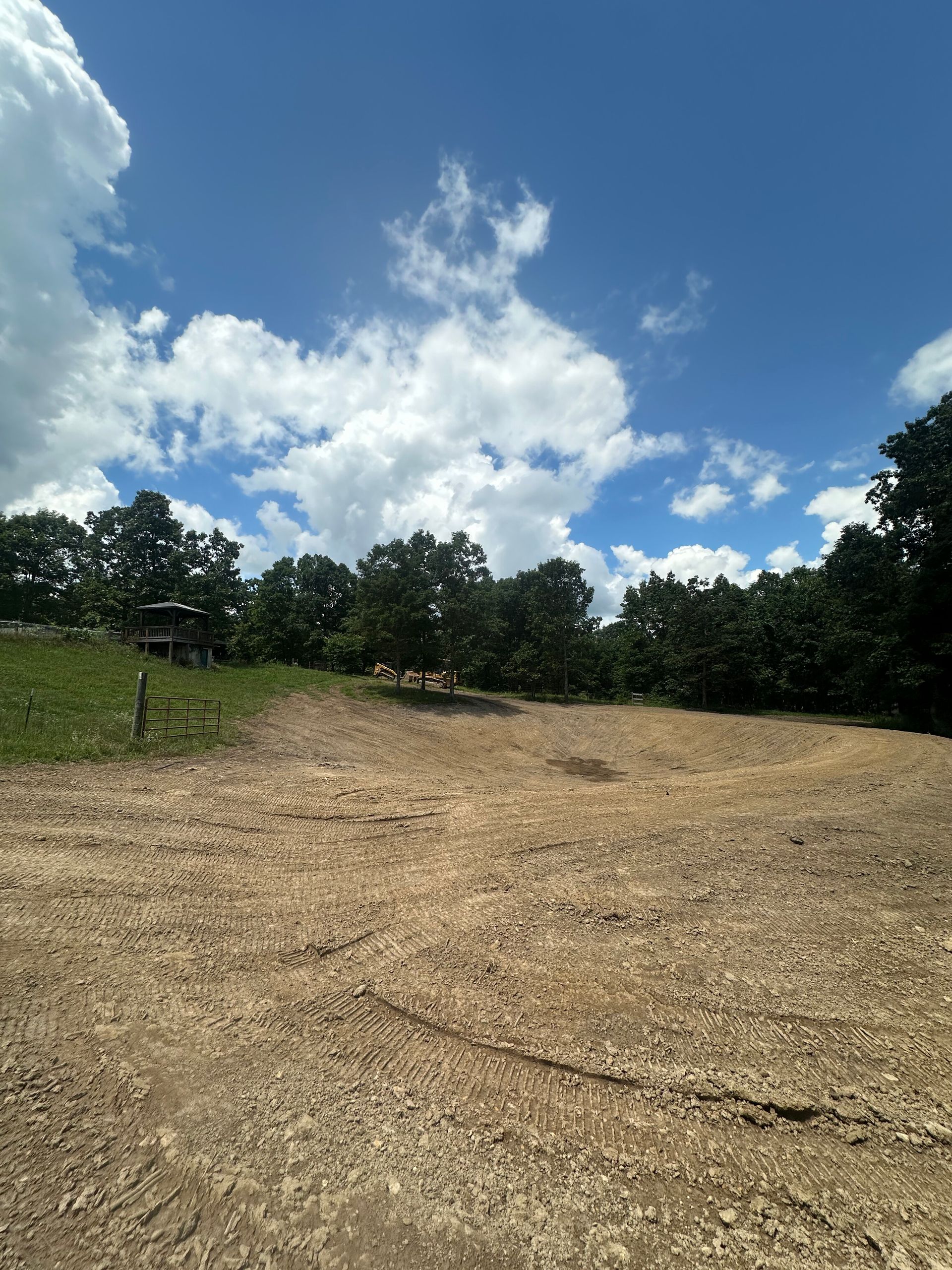 Gravel clearing under a bright blue sky, with trees lining the horizon and white clouds overhead