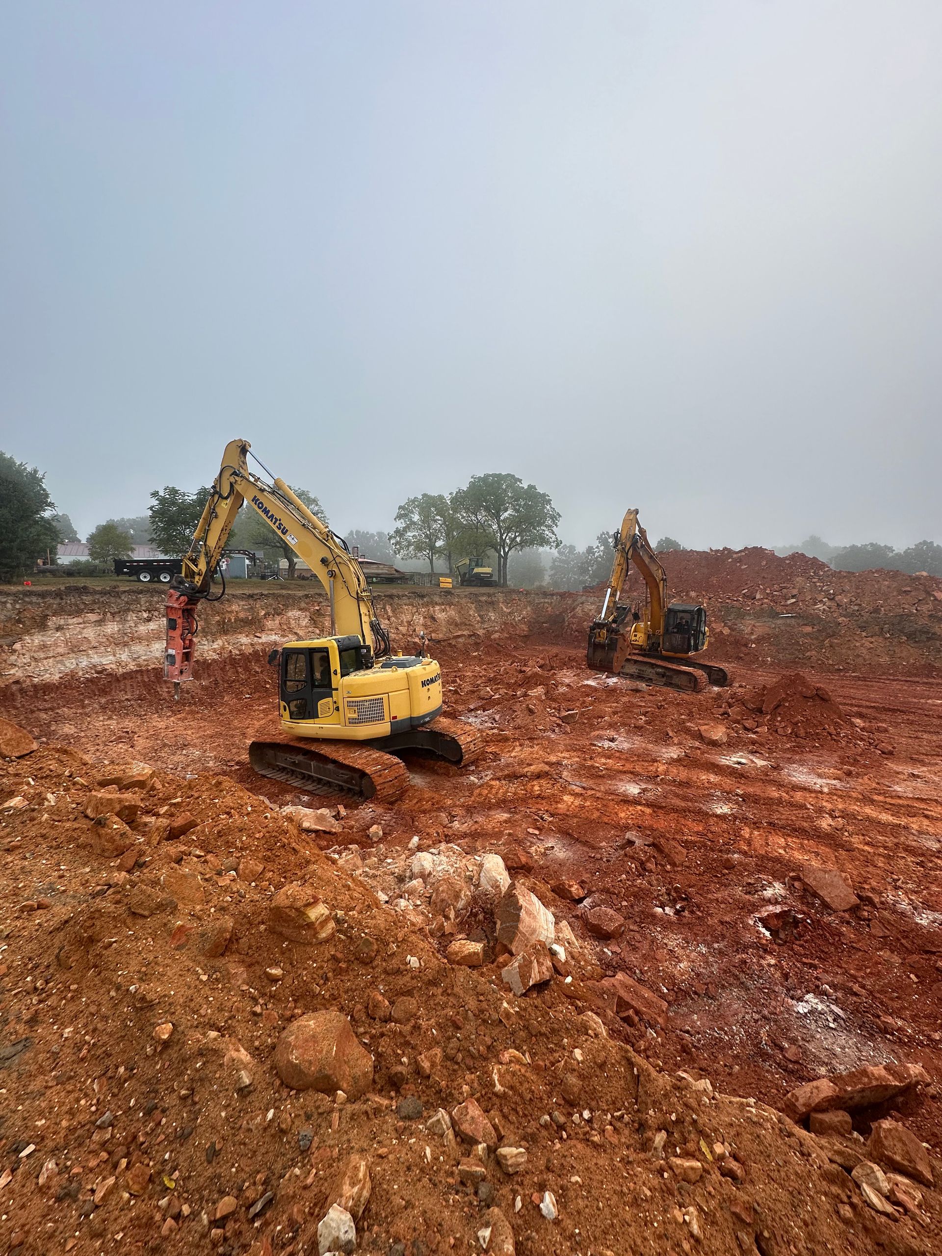 Two excavators working on a muddy construction site under a gray sky.