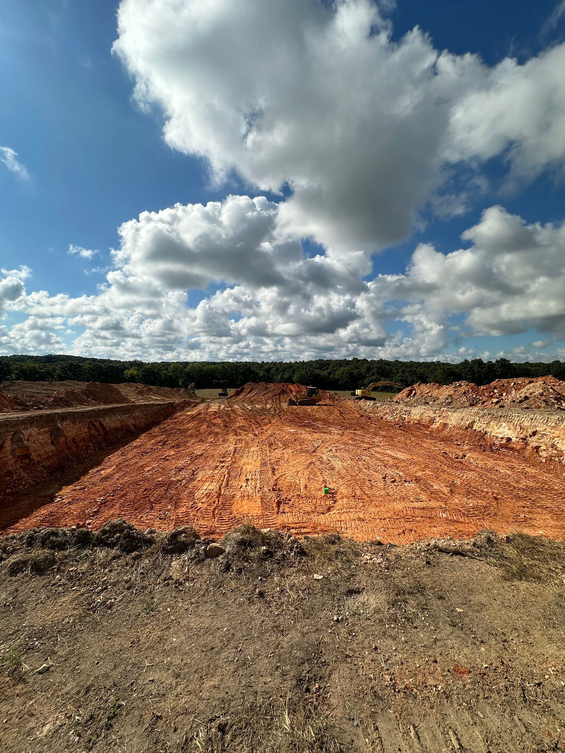 Freshly cleared red dirt lot under a bright blue sky with large white clouds
