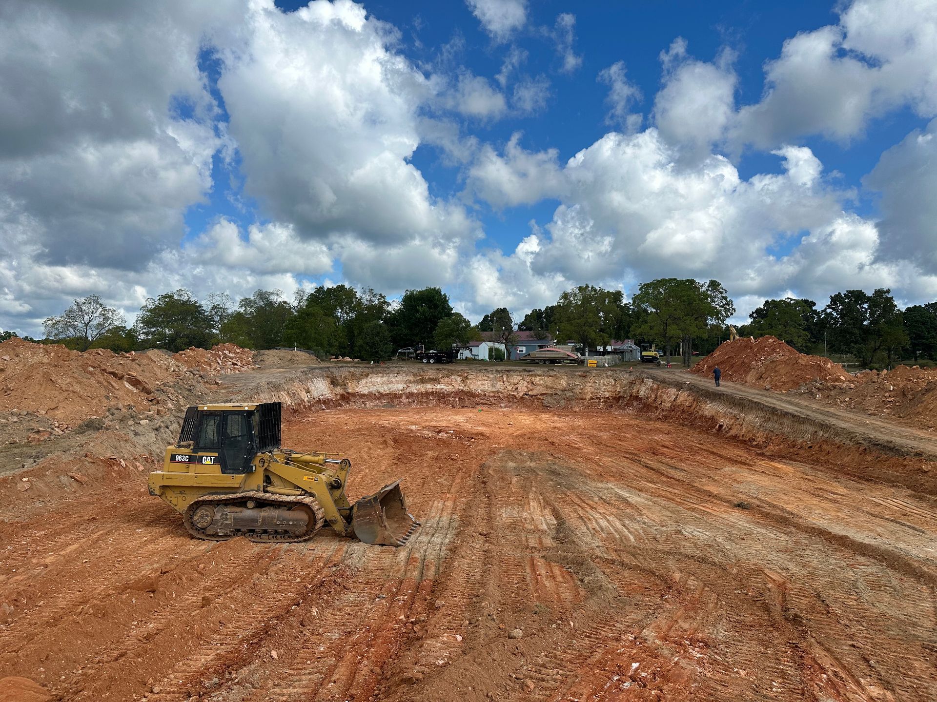 Bulldozer grading a muddy construction site under a cloudy blue sky