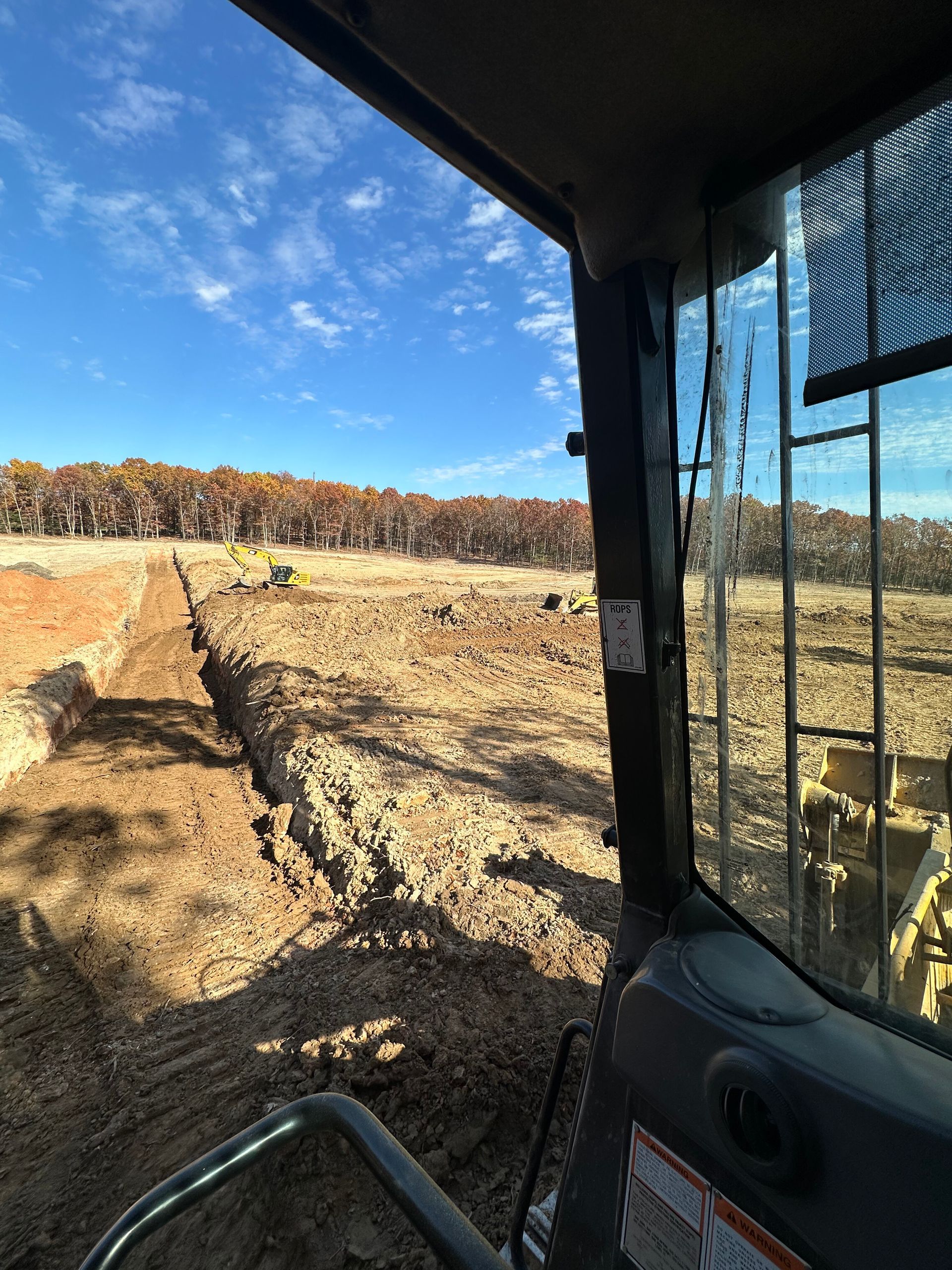 Inside a tractor cab overlooking a dirt field under a blue sky with clouds.