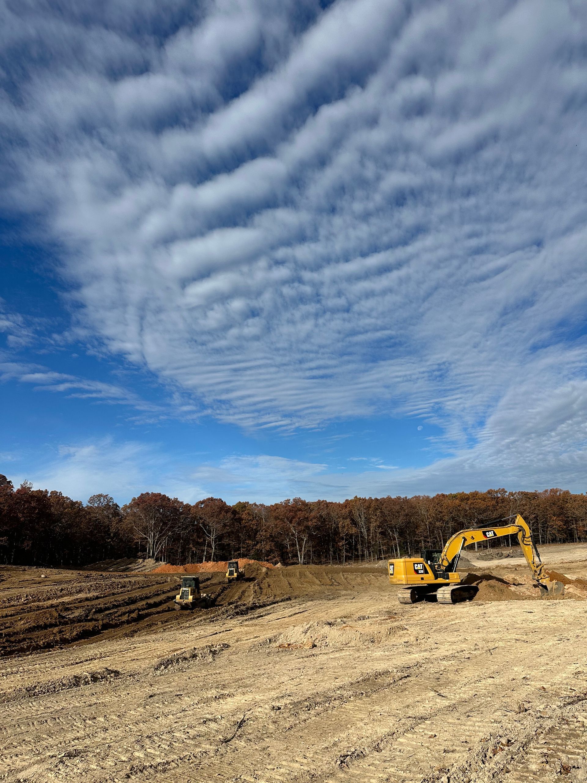 Yellow excavator working on a dirt field under a dramatic cloudy sky