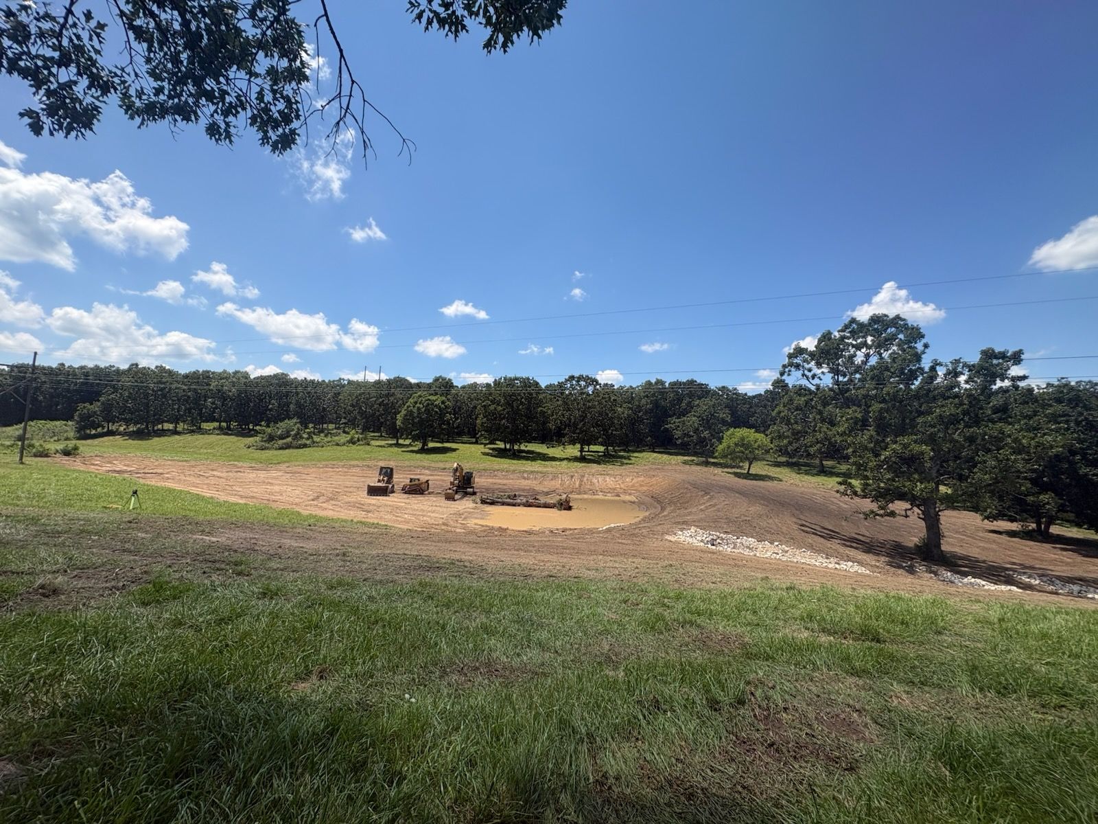 Dry, open field with a few people near a fire pit under a blue sky and trees in the background