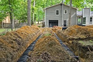 Excavated yard with trenching, black drainage pipe, and a gray house in the background