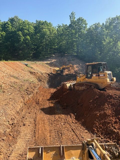 Bulldozer grading a red dirt excavation site with trees in the background