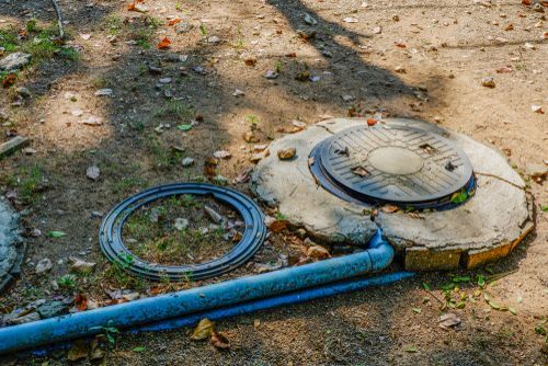 Blue pipe and circular manhole cover on dirt ground with leaves and shadows