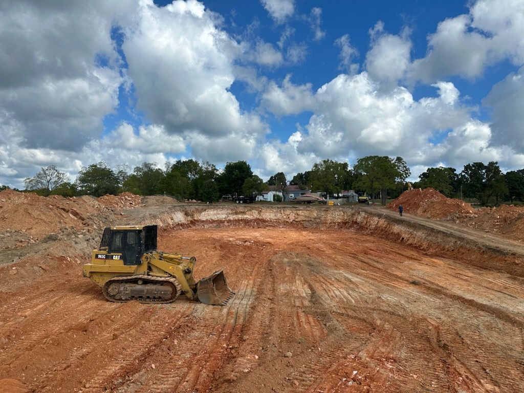 Yellow bulldozer grading a large dirt construction site under a cloudy blue sky