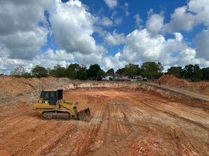 Yellow bulldozer grading a red dirt construction site under a cloudy sky