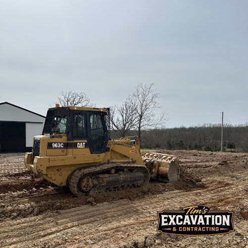 Yellow Caterpillar bulldozer pushing muddy soil at a construction site beside a building